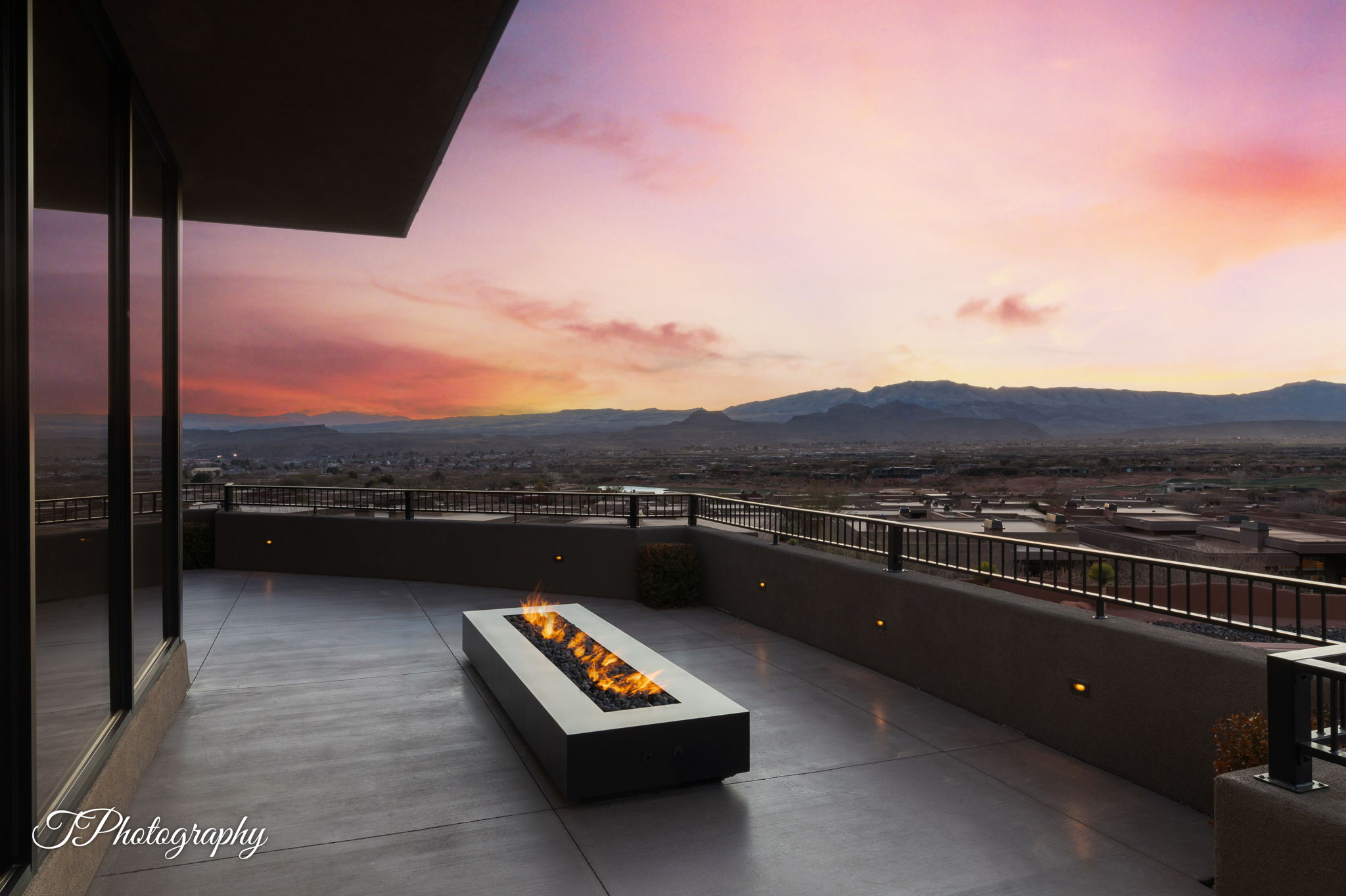 Expansive outdoor terrace featuring a built-in linear fire pit, concrete flooring, and full-height glass panels