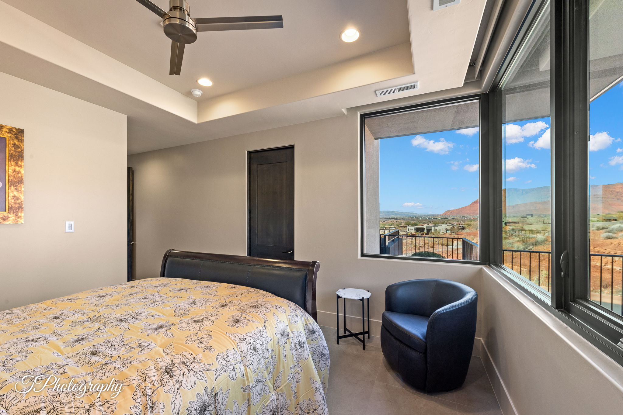 Expansive windows offering panoramic desert and mountain scenery, complemented by a contemporary ceiling fan, recessed lighting, and tray ceiling