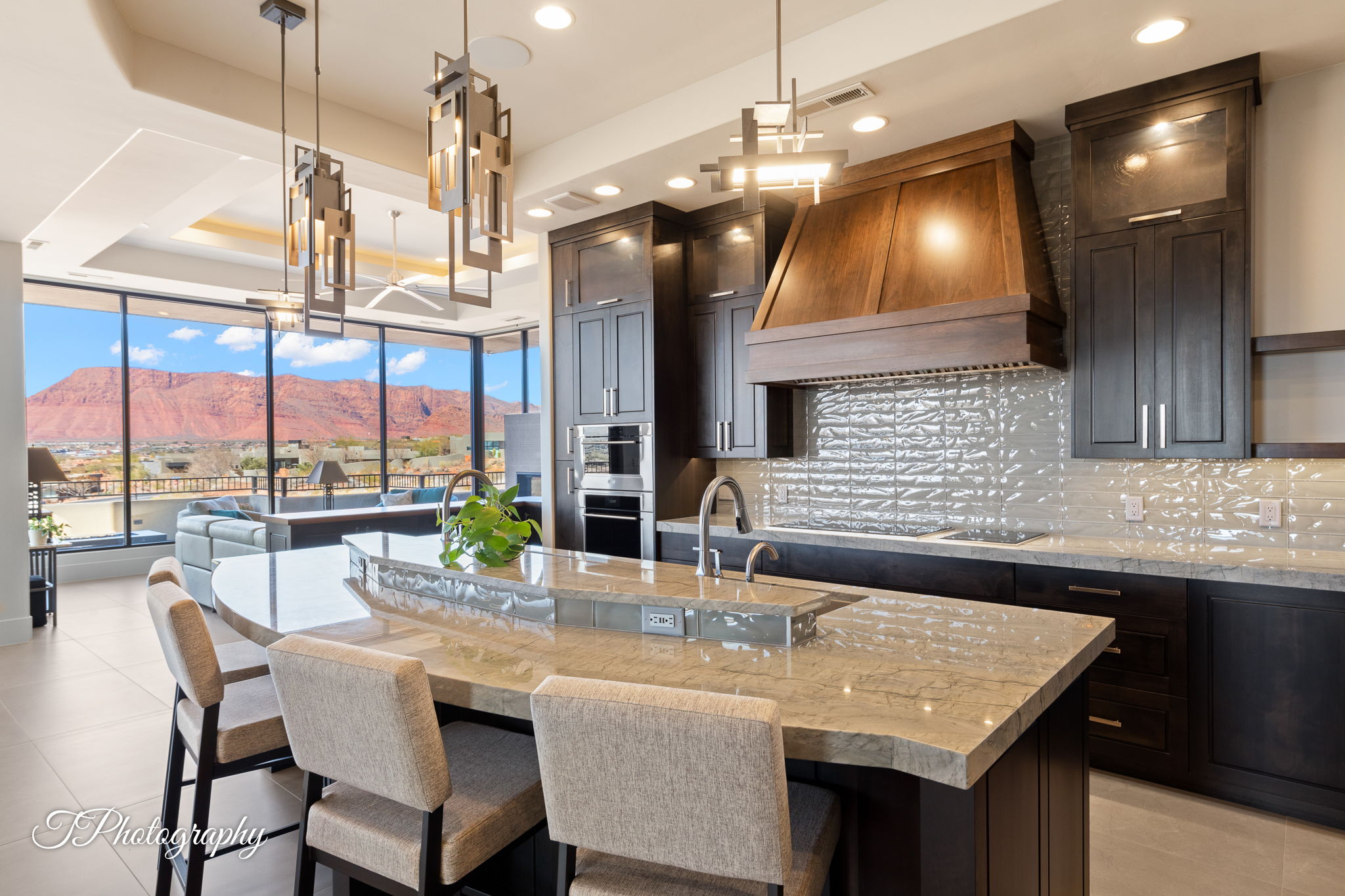 Gourmet kitchen featuring a large island with stone countertop, dark wood-finish cabinetry, stainless steel appliances, and a unique textured backsplash