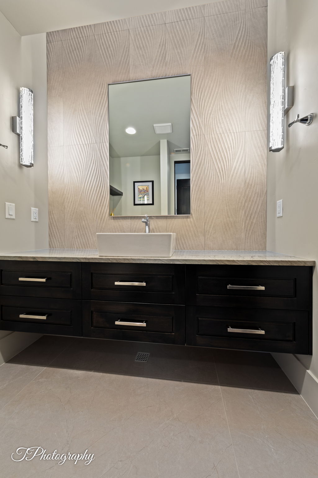 Floating vanity with dark wood-finish cabinetry and chrome hardware, featuring a rectangular vessel sink and light-toned countertop