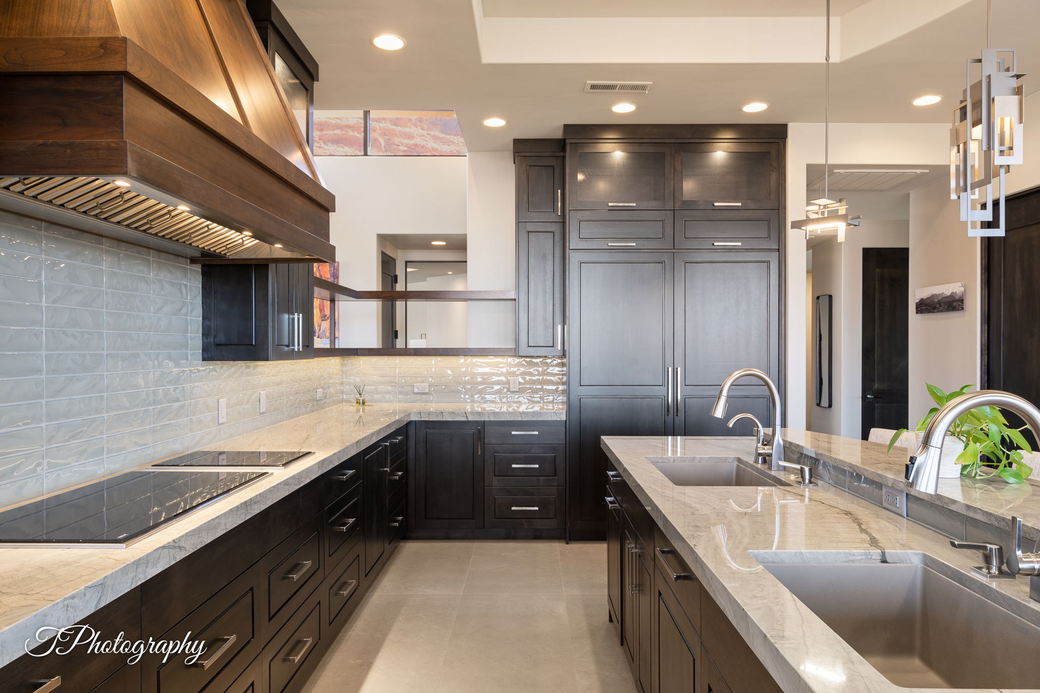 Gourmet kitchen featuring dark wood cabinetry, light-toned countertops, a built-in cooktop, a wood-finish range hood, and integrated appliances