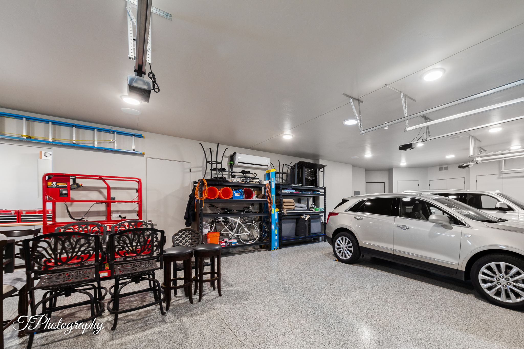 Spacious garage with light gray speckled flooring, white walls, multiple recessed ceiling lights, and two garage door openers