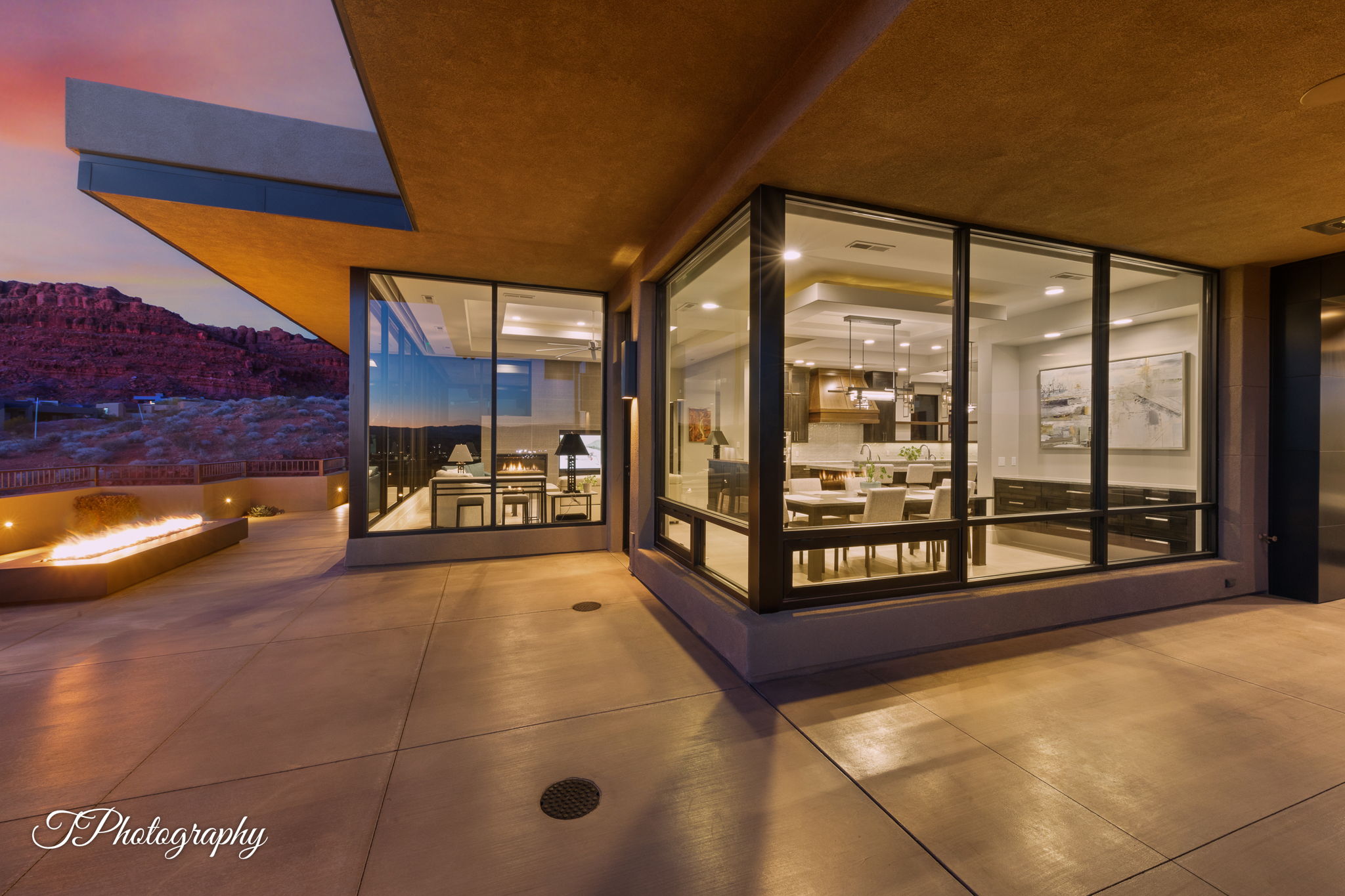 Concrete patio featuring a linear fire pit, complemented by an exterior of brown stucco with dark-framed windows