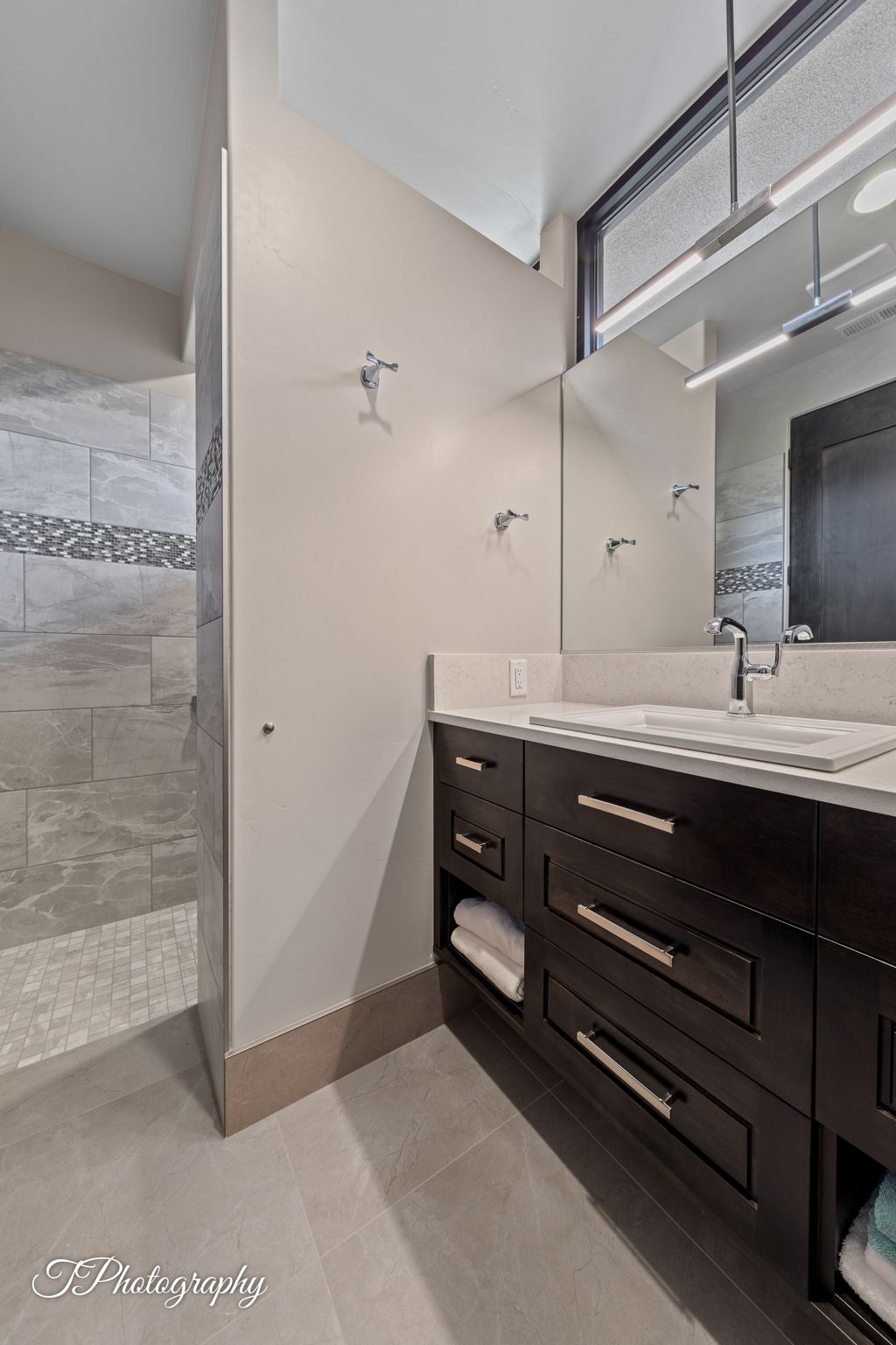 Dark wood vanity featuring a built-in rectangular sink, light-toned countertop, and contemporary pull hardware