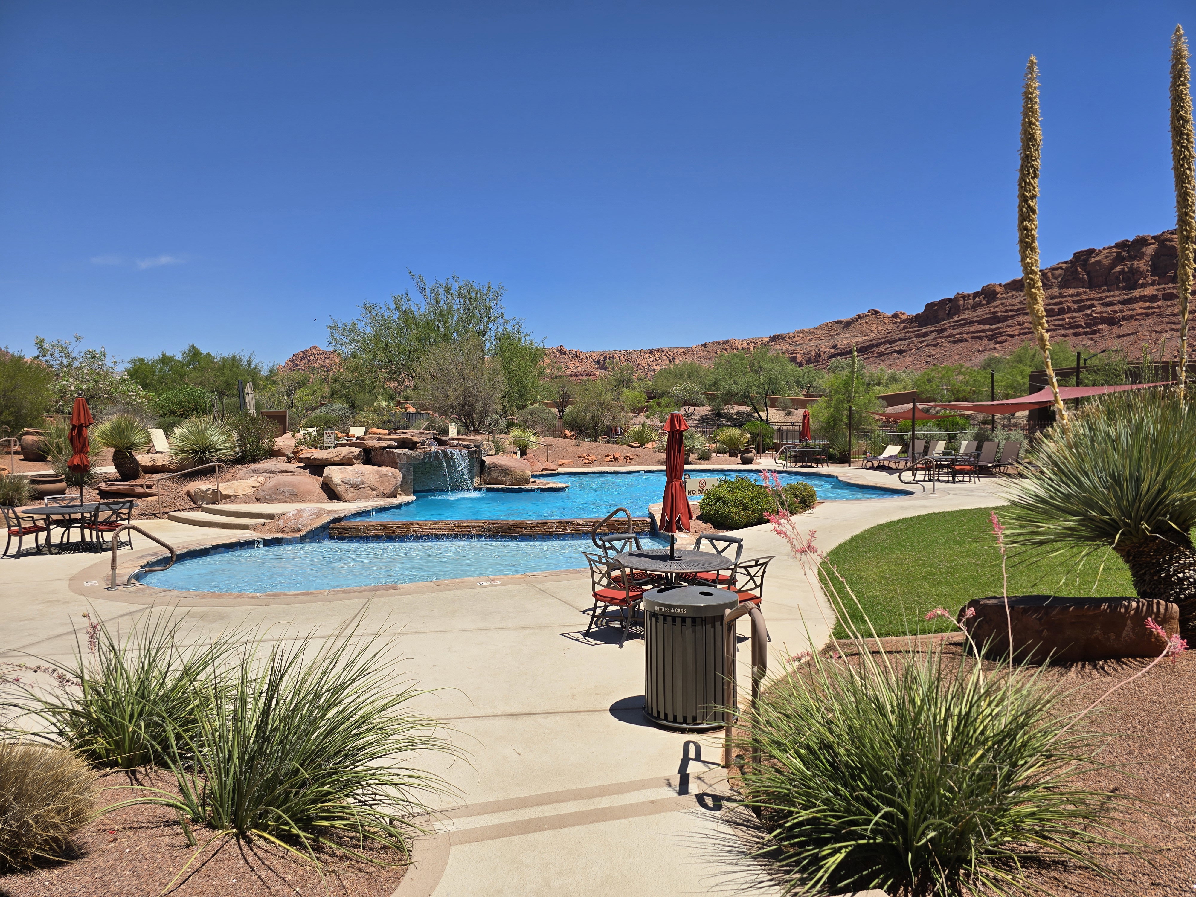 Custom-shaped swimming pool with an integrated rock waterfall feature, surrounded by a concrete deck with desert landscaping