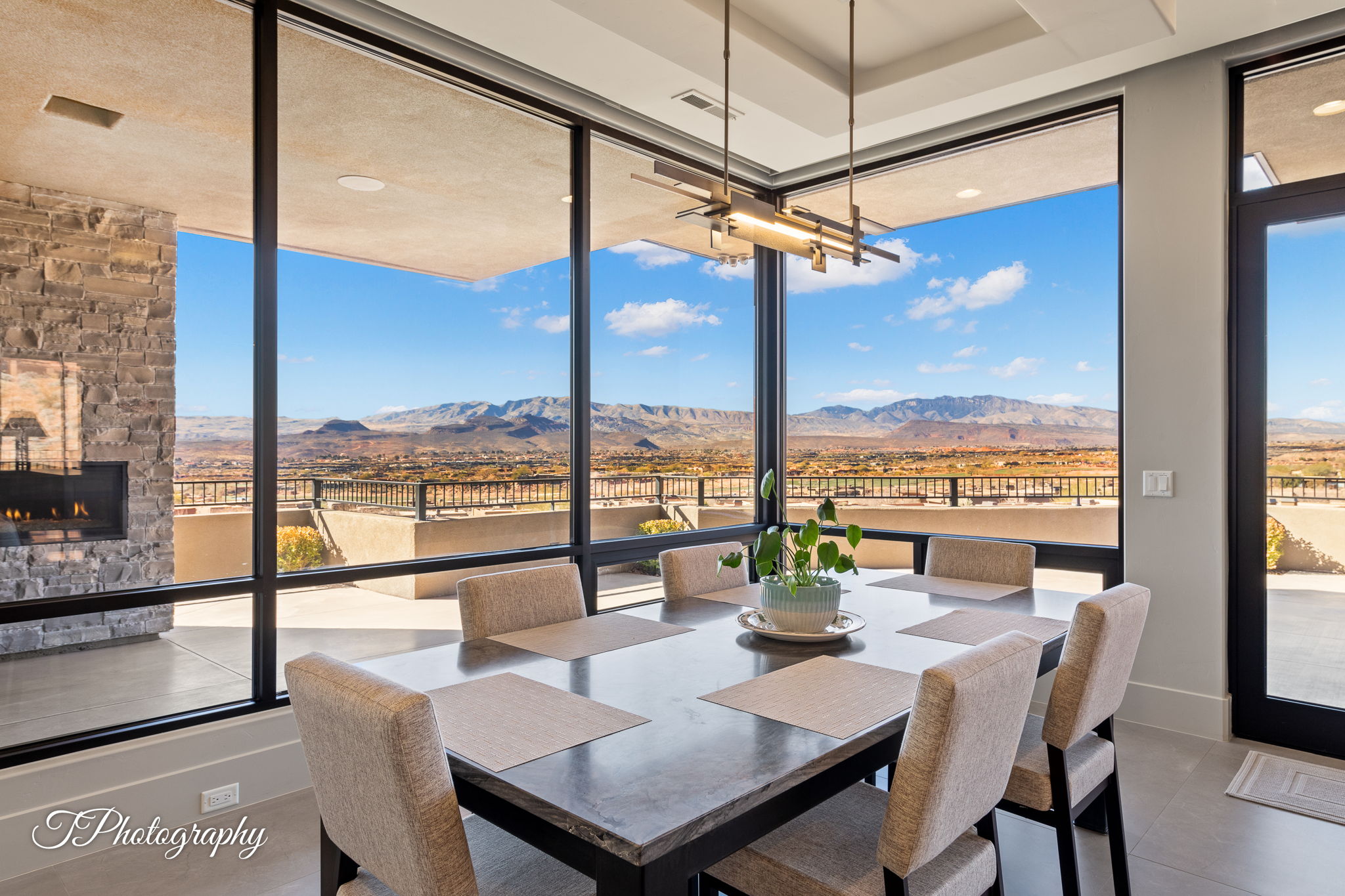 Dining area featuring expansive window walls, a linear chandelier, a stone-clad fireplace, and tile flooring
