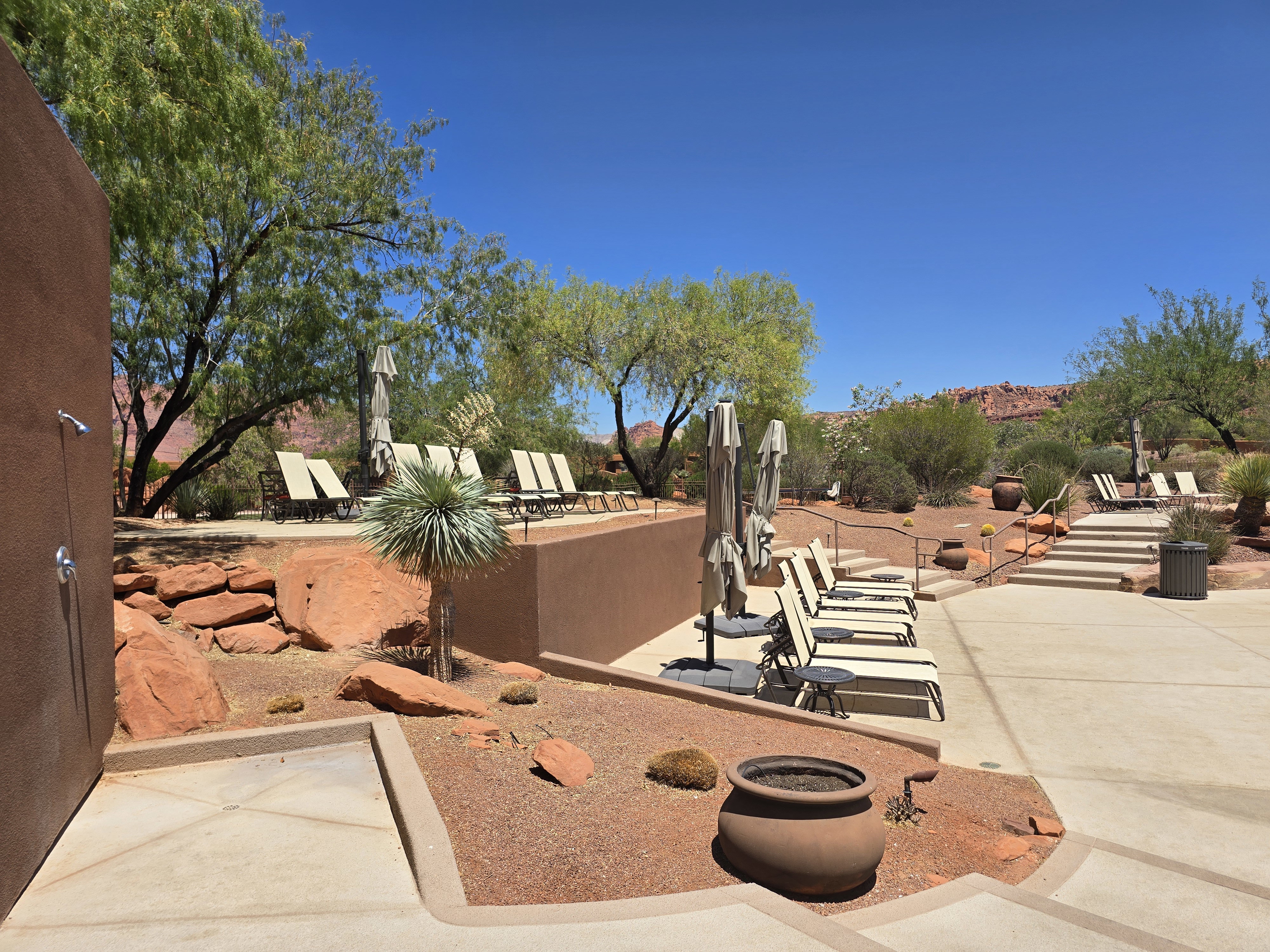 Outdoor pool area featuring desert landscaping with red rock accents and mature trees
