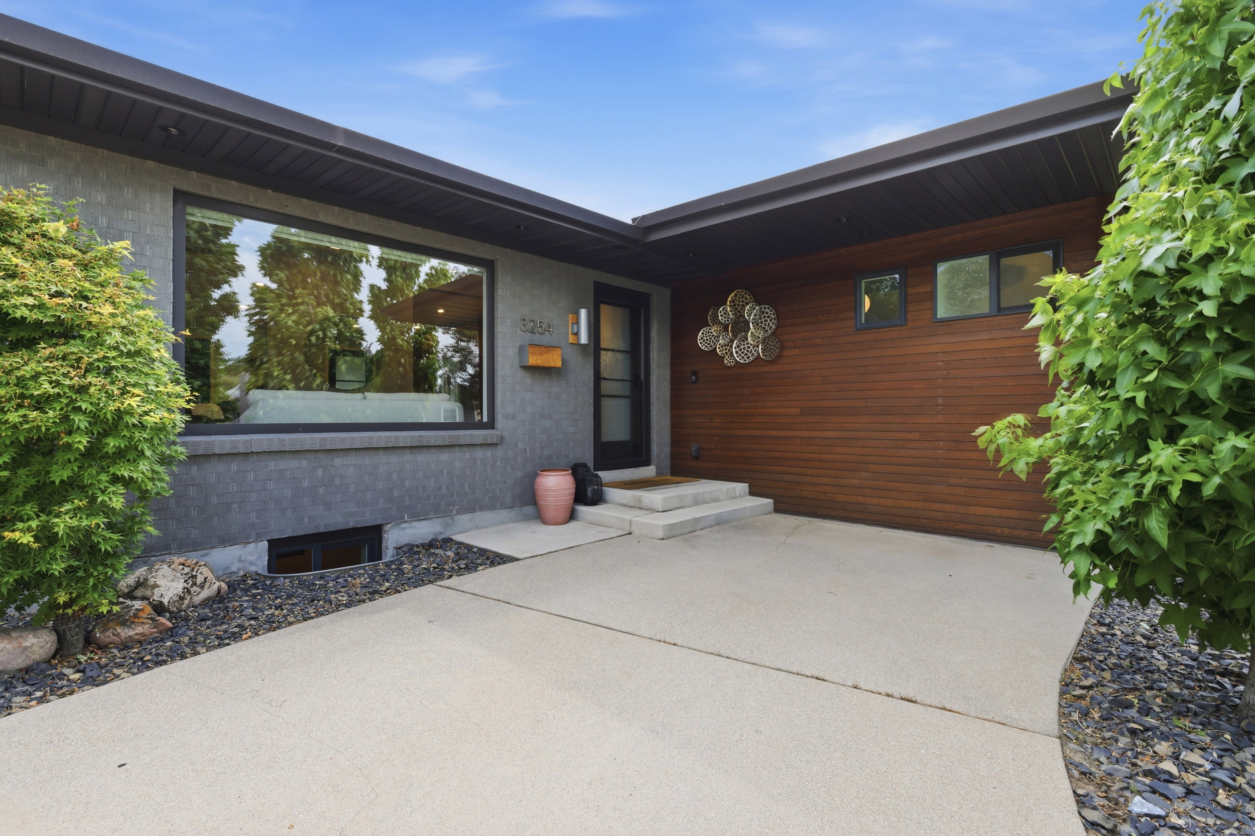 Modern exterior featuring a prominent picture window, dark grey brickwork, wood-finish siding, and a concrete pathway