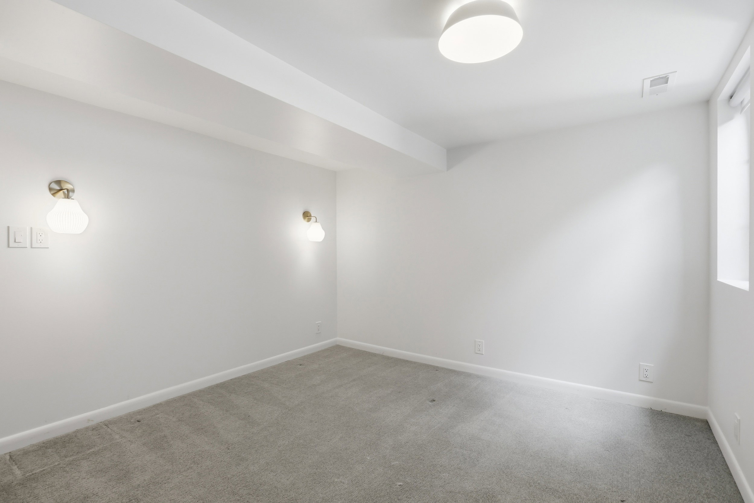 Room featuring light gray carpeting, crisp white walls, a flush-mount ceiling light, and two sconce light fixtures