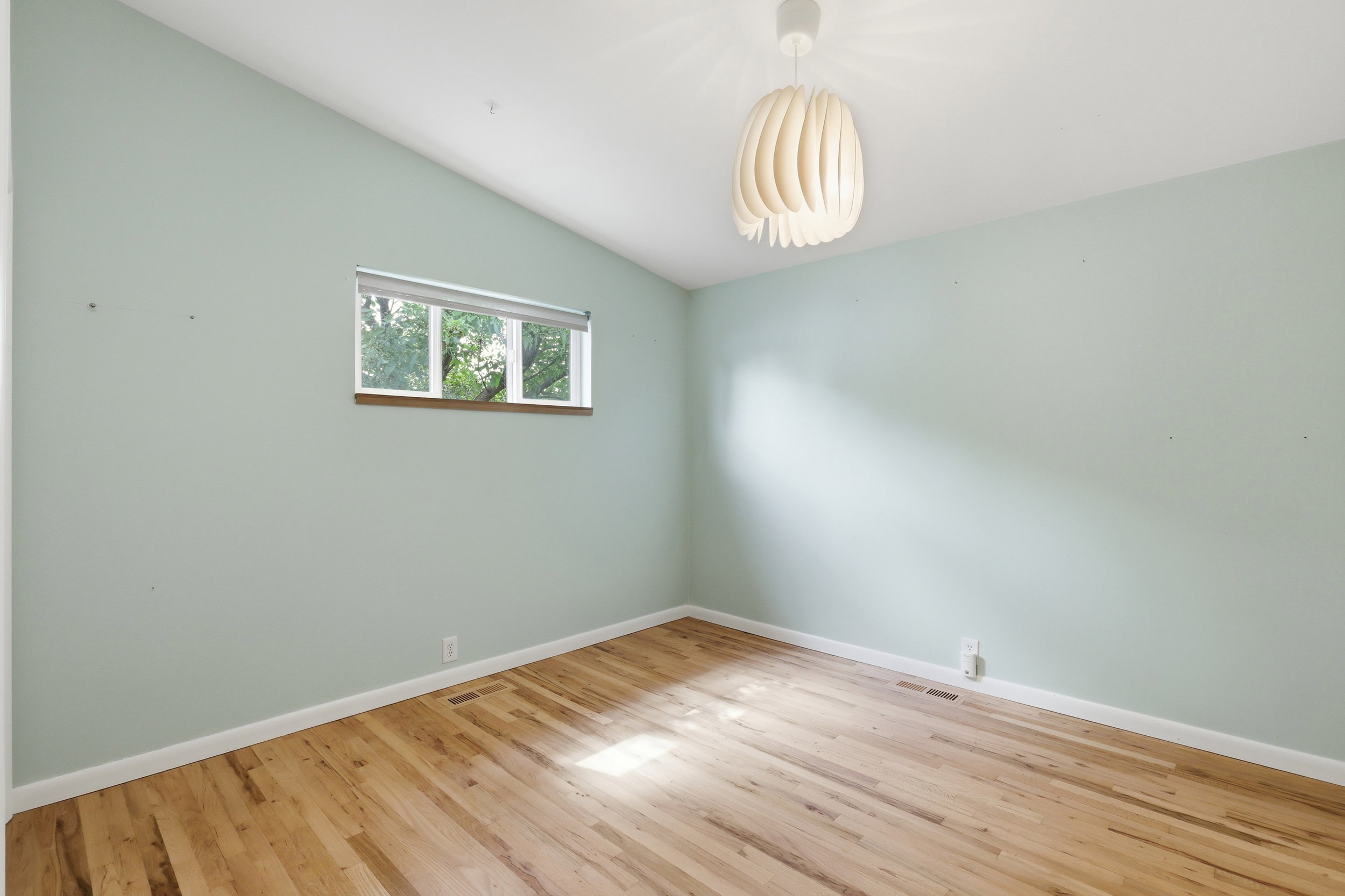 Room featuring wood-finish flooring, a contemporary pendant light fixture, a vaulted ceiling, and a window with a wood sill
