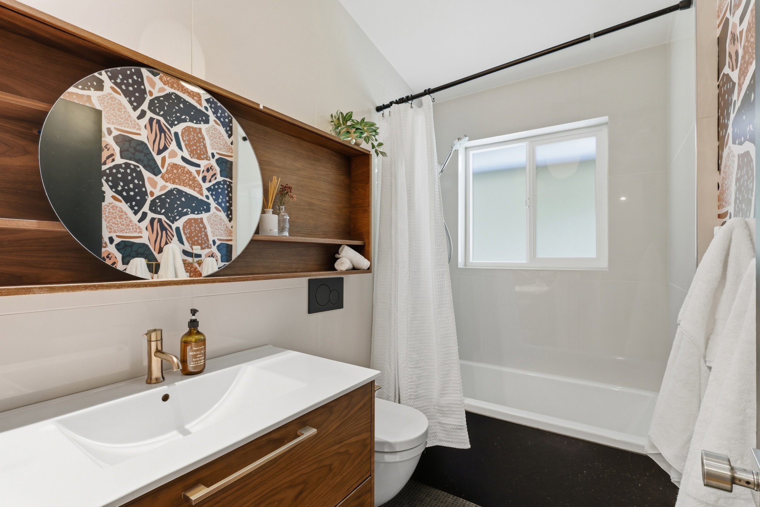 Bathroom featuring a wood-finish vanity with a white integrated sink, a round mirror, and a built-in wood-finish shelving unit