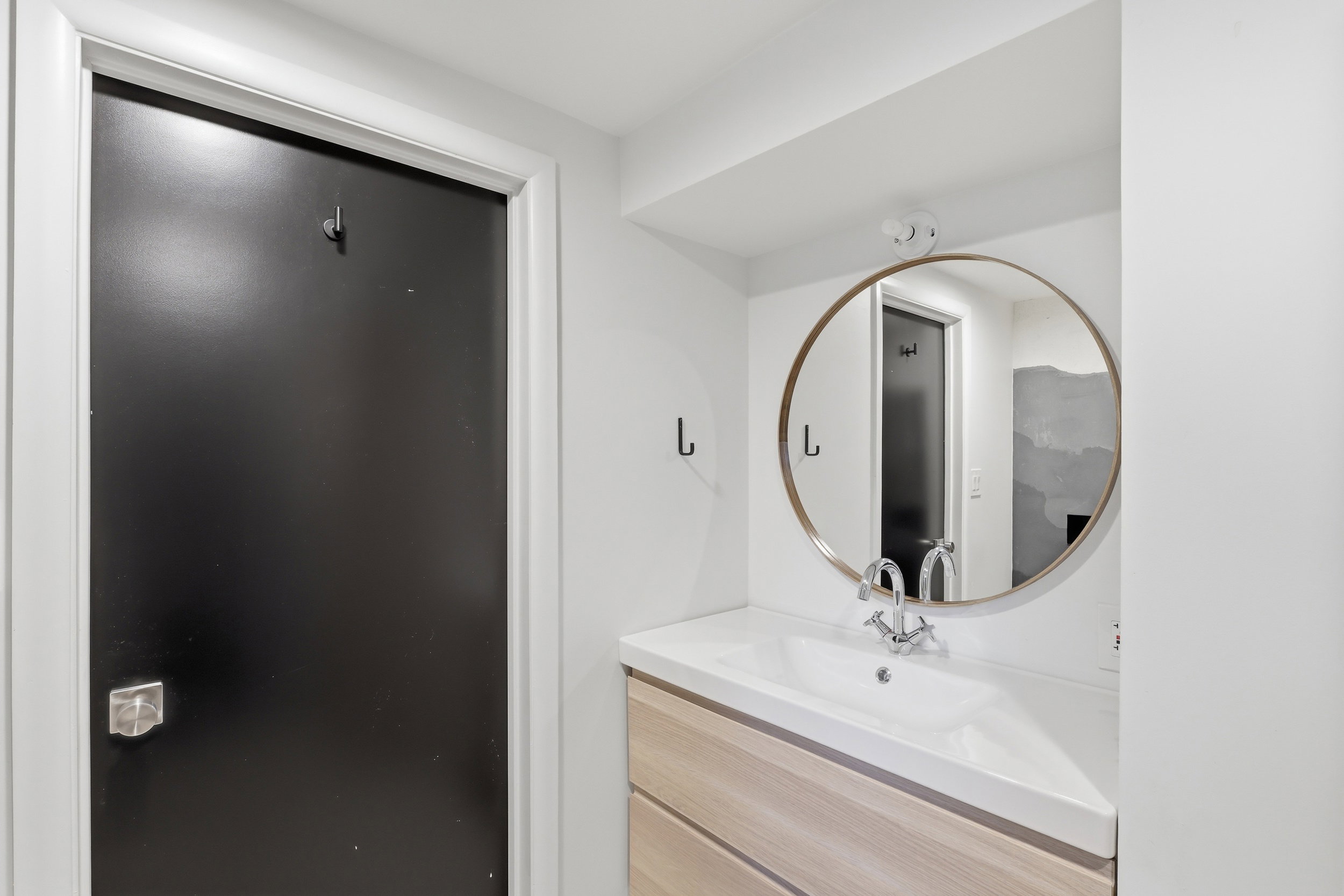 Vanity featuring a white integrated sink with a chrome faucet, wood-finish cabinetry, and a circular mirror