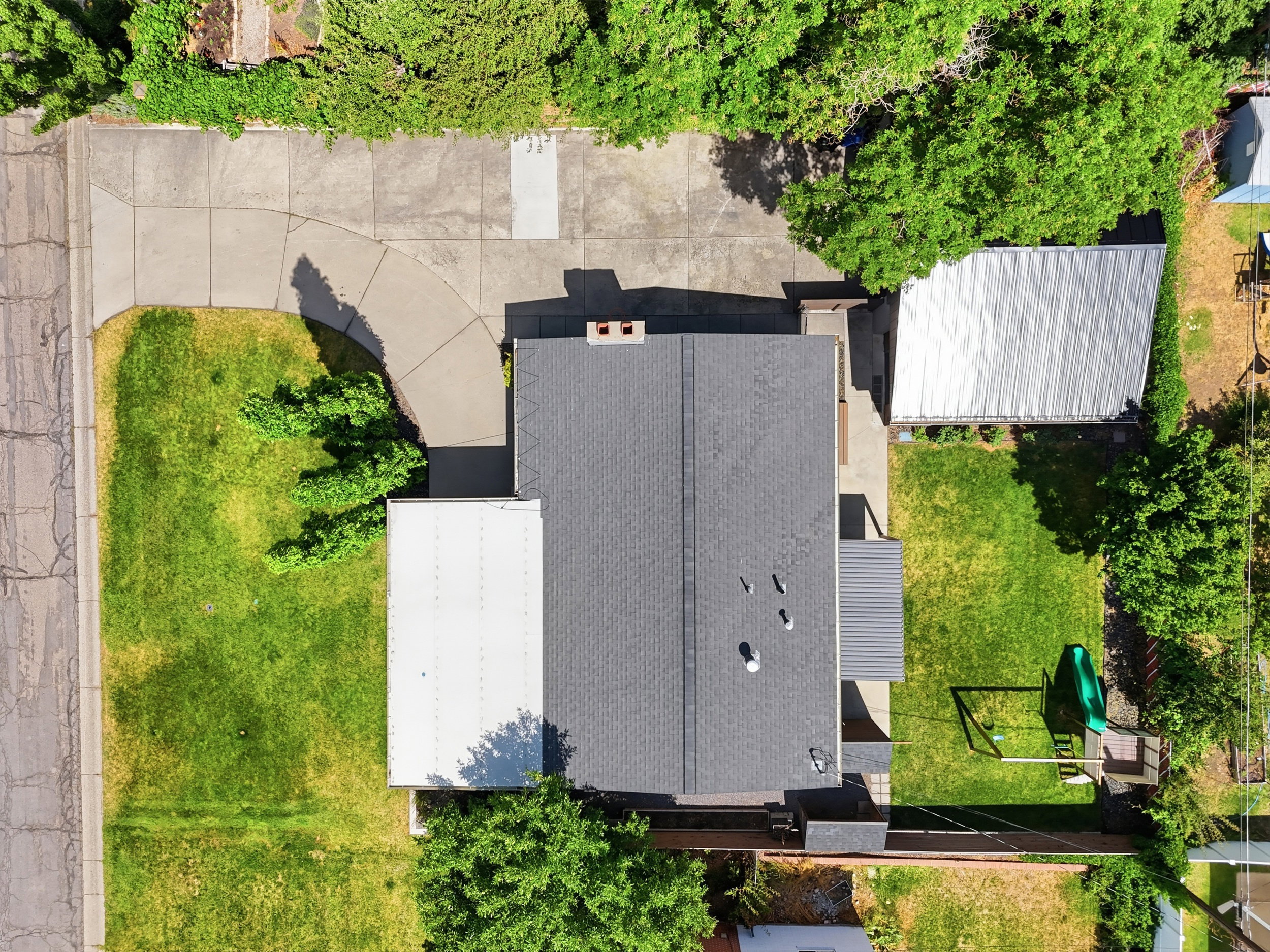 Property featuring a dark shingle roof, a light-colored flat roof section, and a corrugated metal roof structure