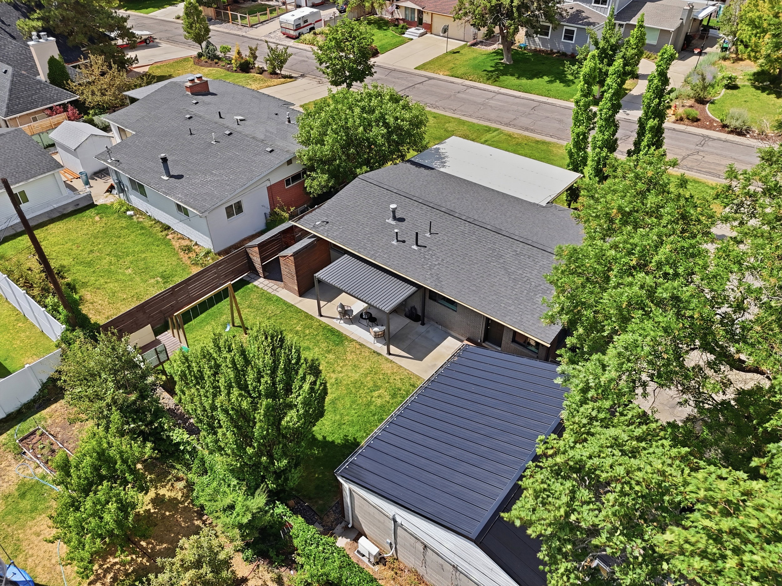 Expansive backyard featuring a manicured lawn, established trees, and a covered patio area