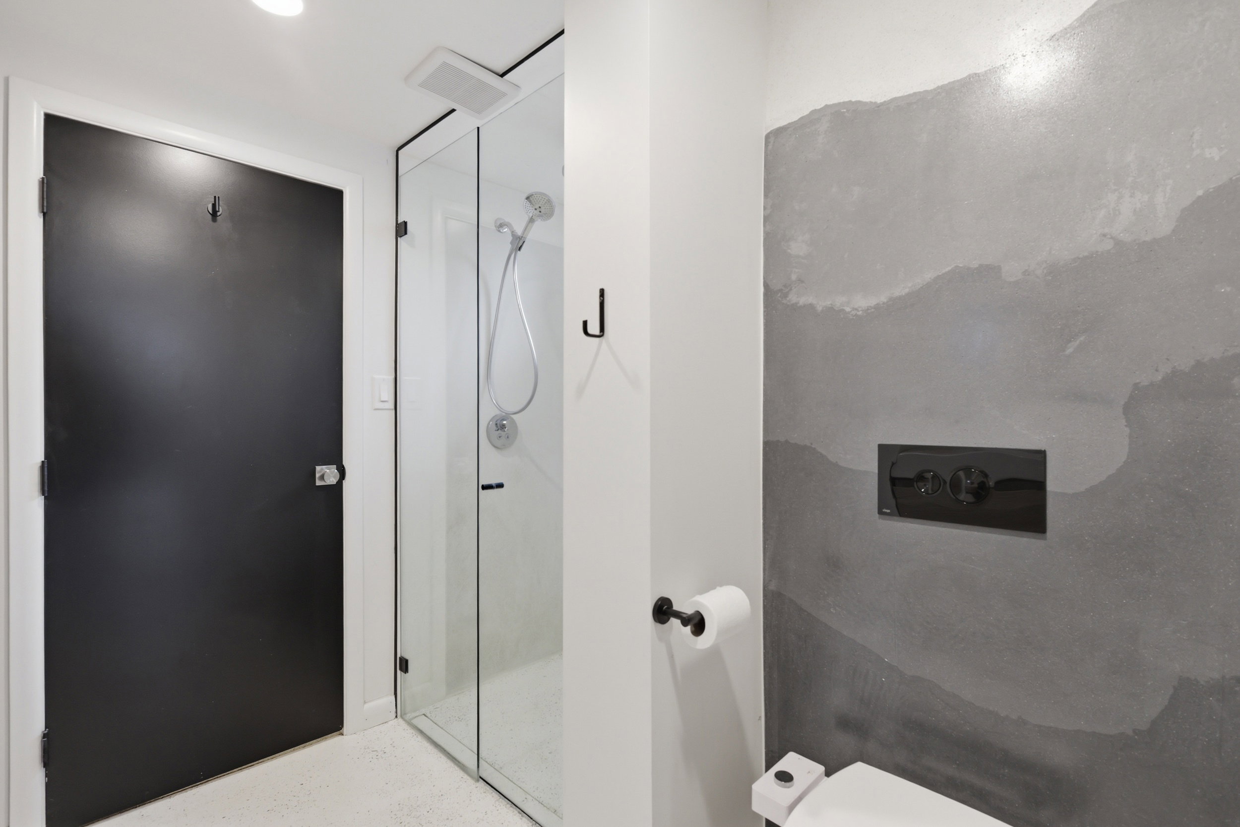 Contemporary bathroom featuring a frameless glass shower enclosure, a wall-mounted toilet with a concealed tank, and a textured accent wall