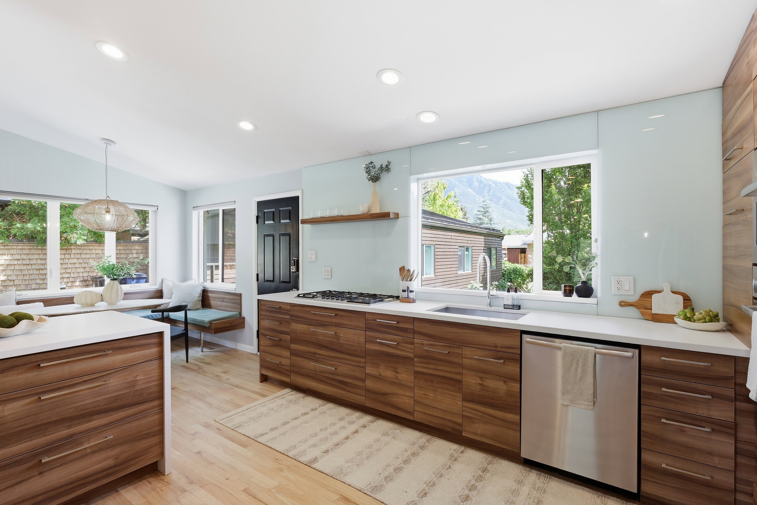 Contemporary kitchen featuring wood-finish cabinetry, light countertops, stainless steel appliances, and a built-in banquette seating area