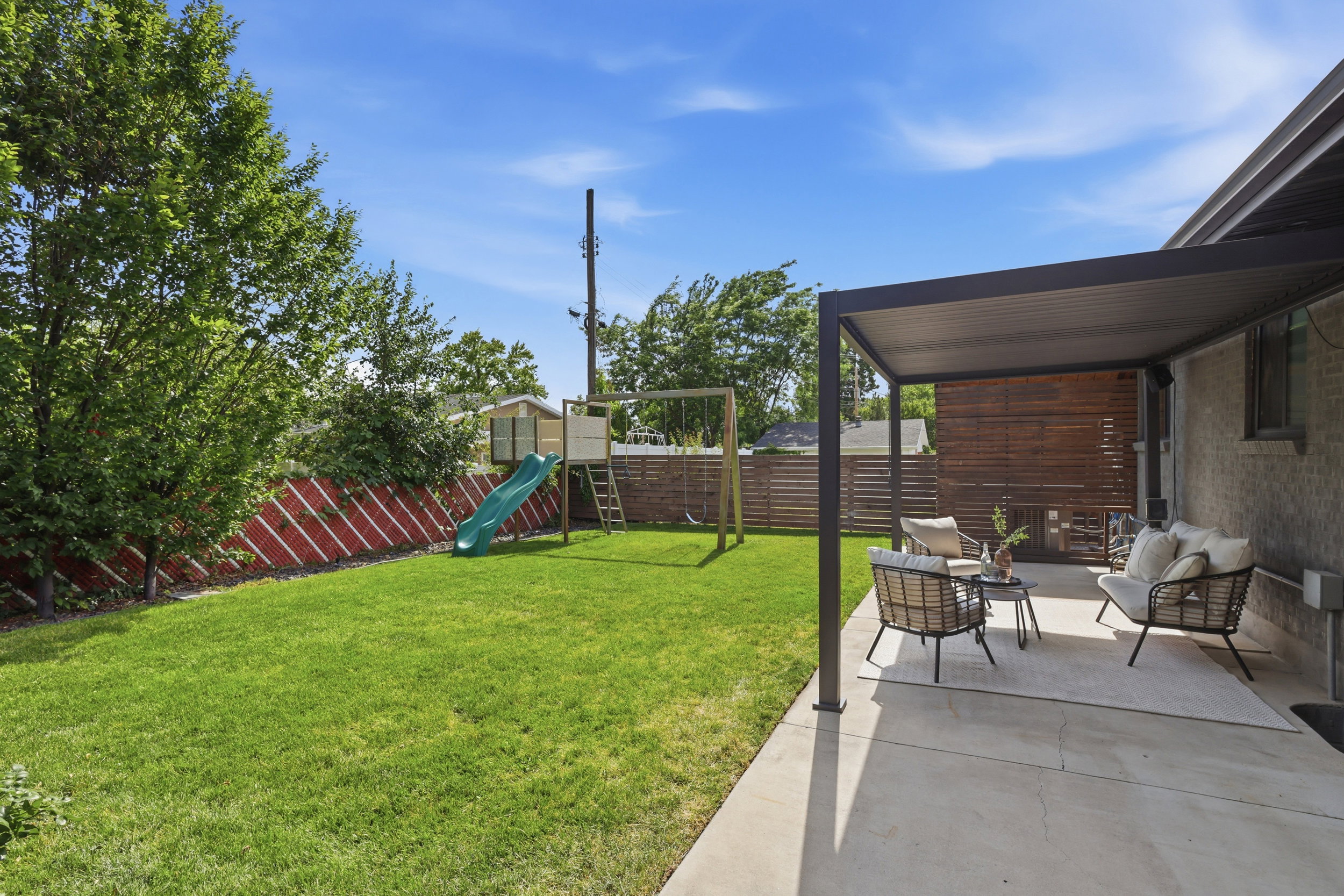 Concrete patio with a modern pergola, leading to a green lawn with a wooden privacy fence