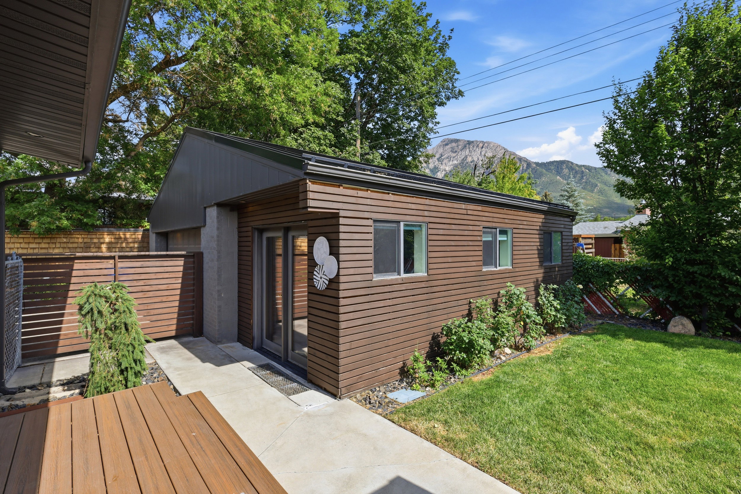 Modern accessory dwelling unit featuring horizontal wood-finish siding, multiple windows, a concrete walkway, and an adjacent grassy area