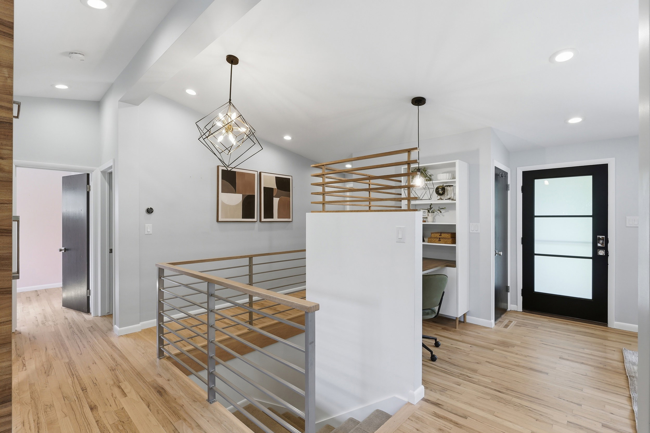 Upper-level hallway featuring wood-finish flooring, a contemporary metal and wood railing, recessed lighting, and a built-in shelving unit with desk space