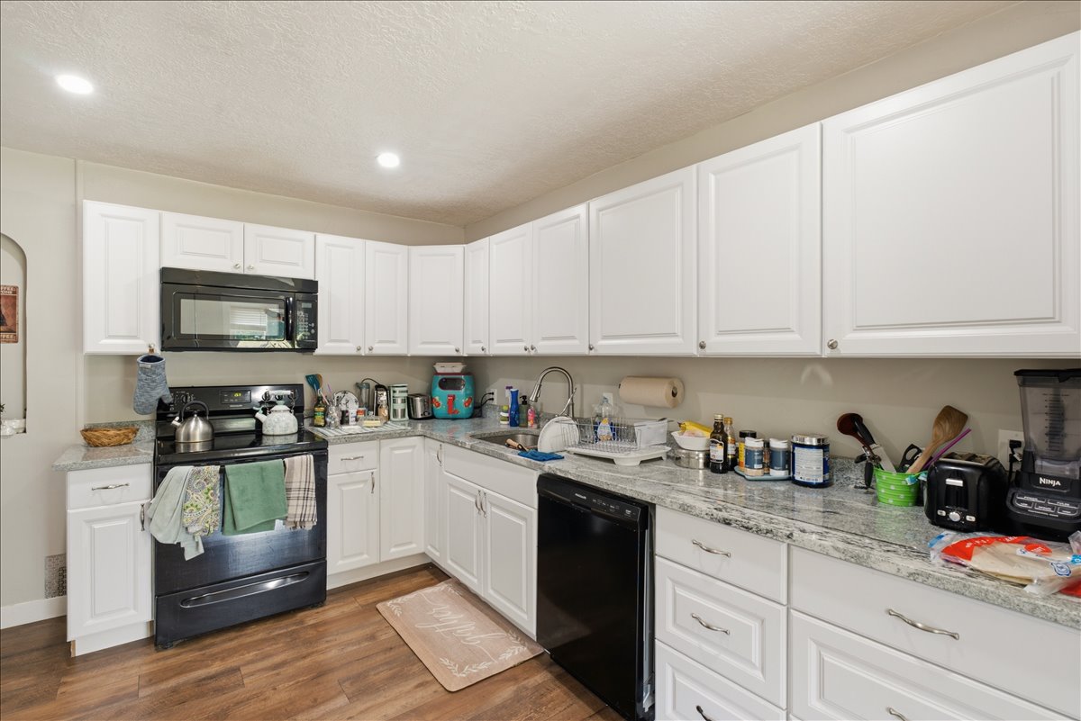 Kitchen featuring white cabinetry, light-toned countertops, a black range with an above-range microwave, a built-in dishwasher, and wood-finish flooring