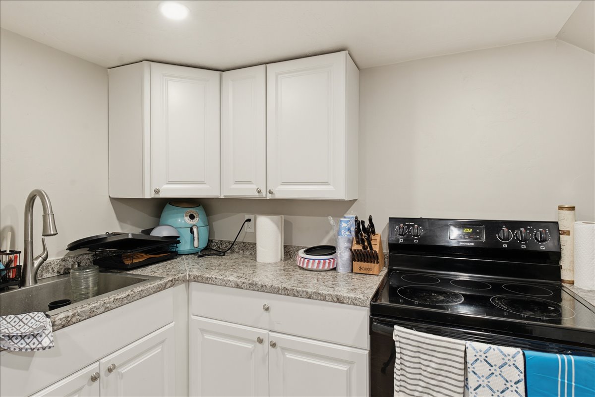 Functional kitchen corner featuring white cabinetry, light-toned countertops, a stainless steel sink with a gooseneck faucet, and a black electric range