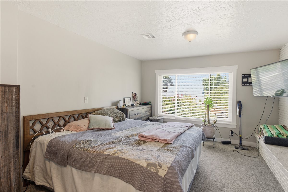 Spacious room featuring light gray walls, textured ceiling, a large window with white blinds and trim, and gray carpeting