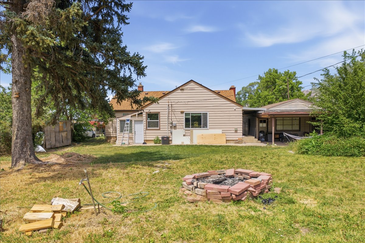 Expansive backyard featuring a brick-lined fire pit, mature evergreen tree, and covered patio space