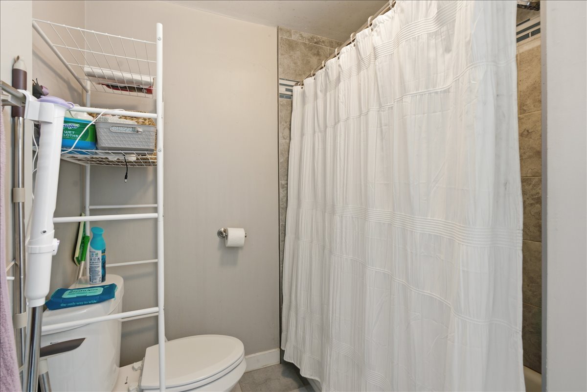Bathroom featuring a white toilet, neutral wall paint, and floor-to-ceiling tiled shower surround
