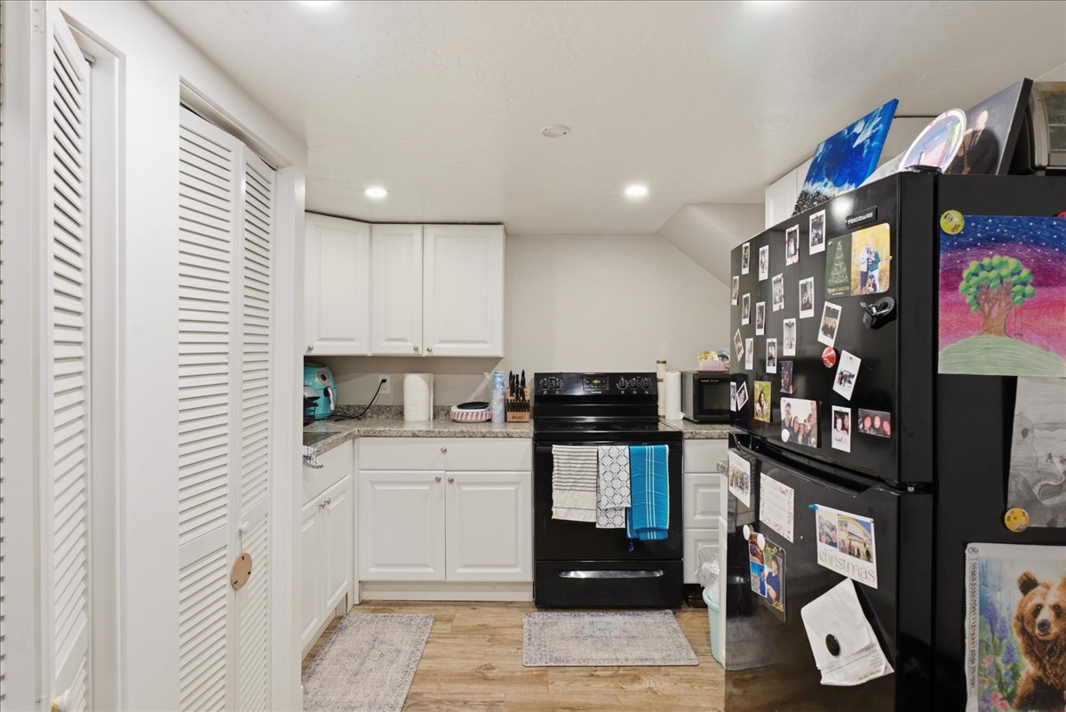 Compact kitchen featuring white cabinetry, light-colored countertops, black appliances, recessed lighting, and wood-finish flooring