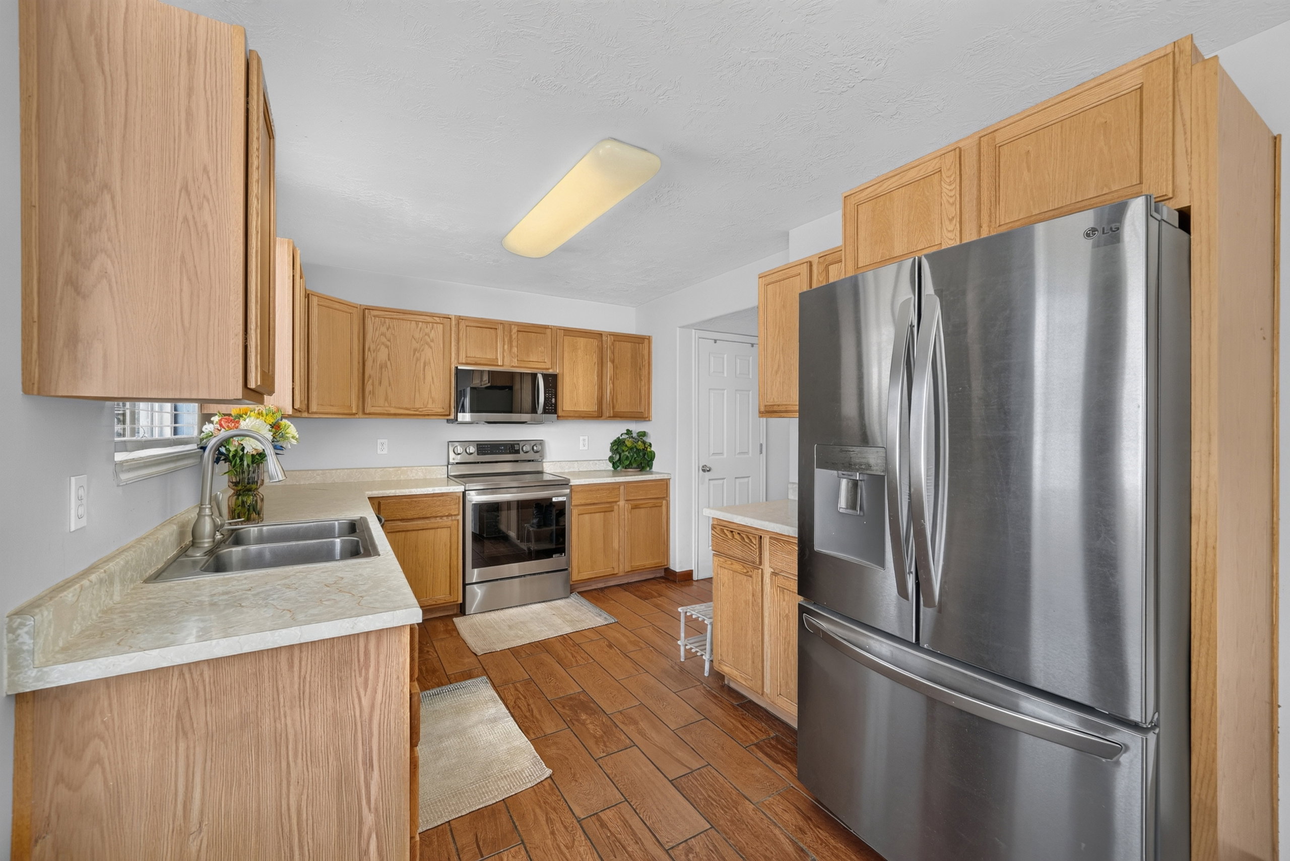 Kitchen featuring wood-finish cabinetry, stainless steel appliances, stone-finish countertops, wood-finish flooring, and a double basin sink