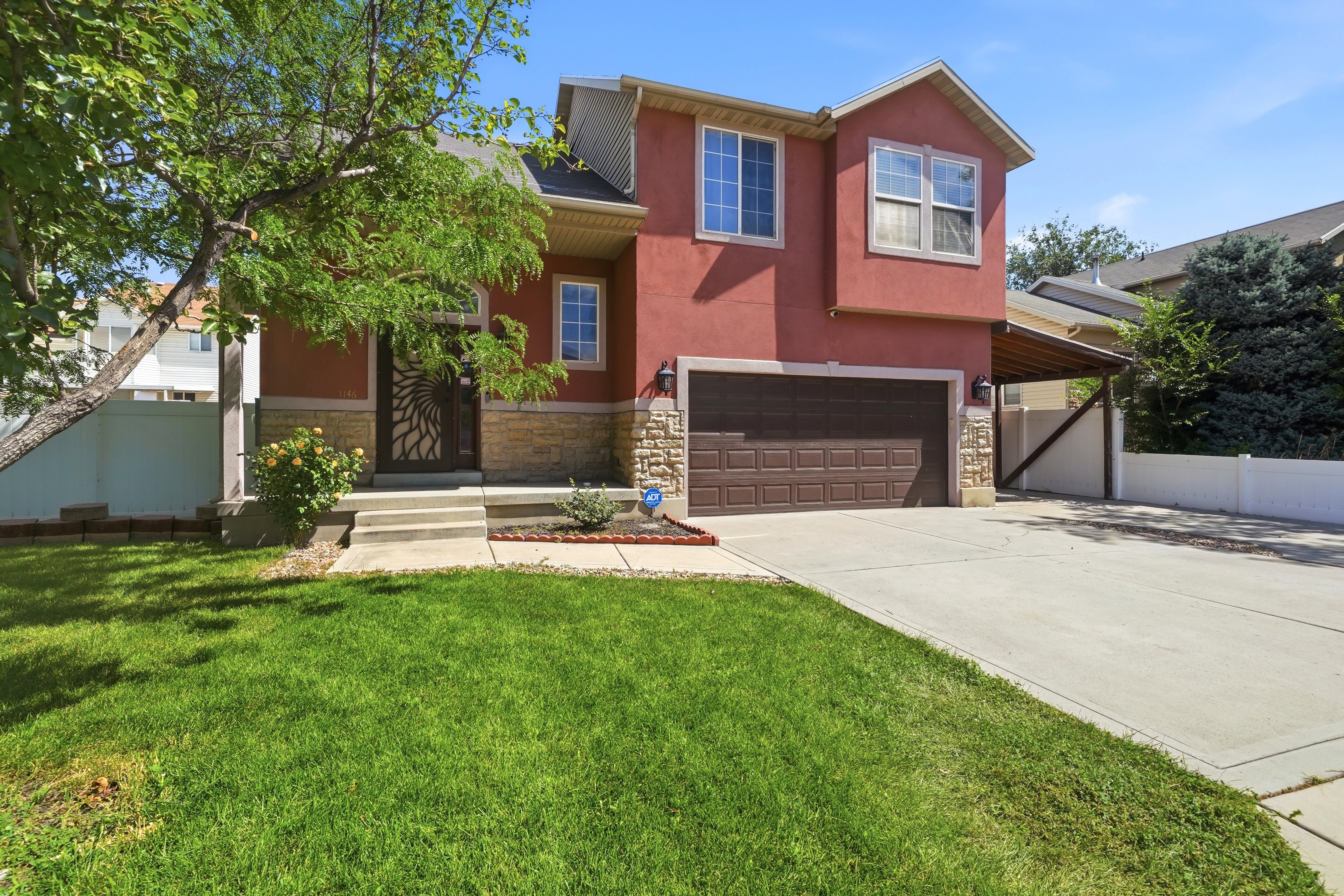 Red stucco exterior with stone accents, a two-car garage, and a covered carport