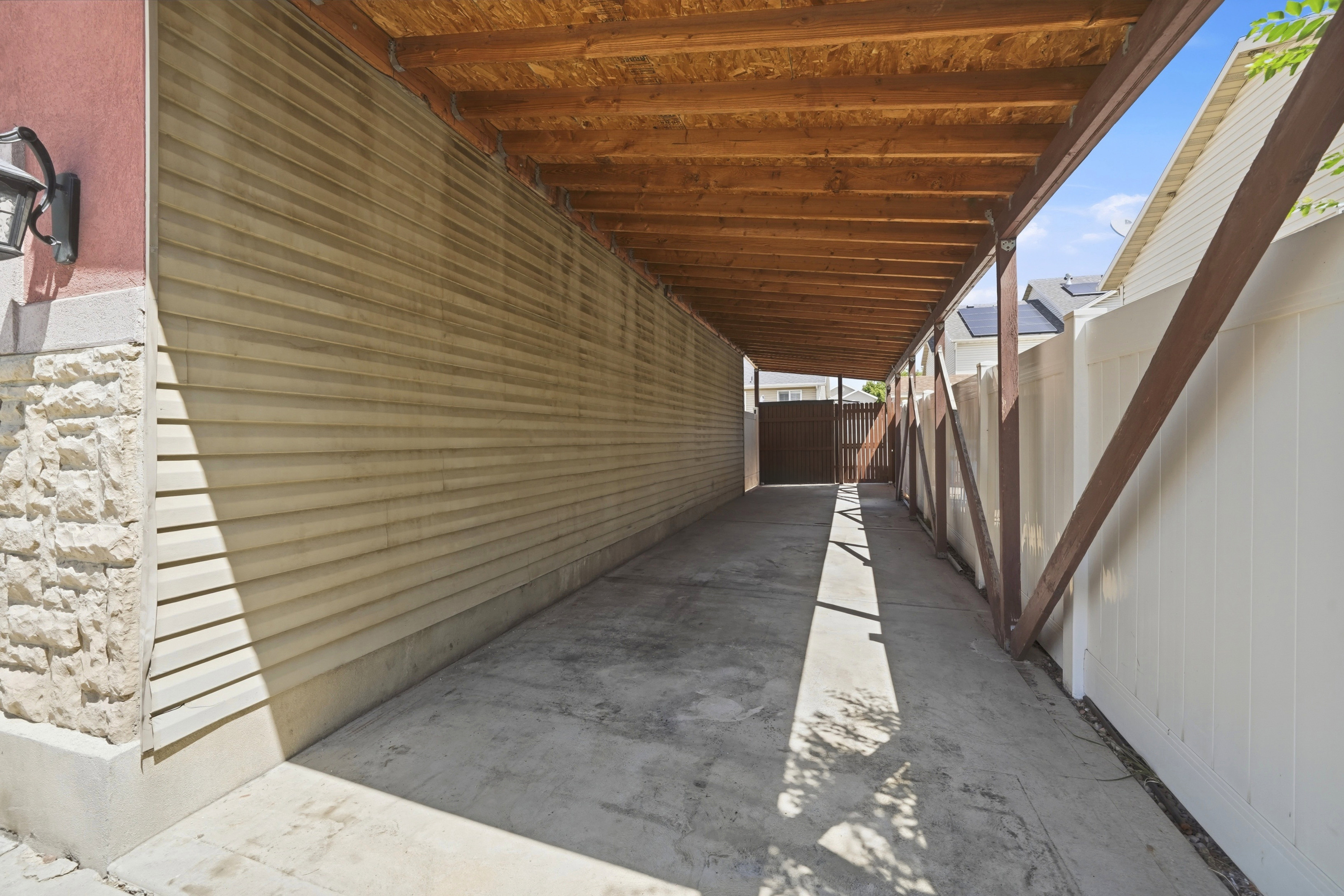 Covered concrete driveway featuring a wood-beam ceiling, vinyl siding, and a privacy fence