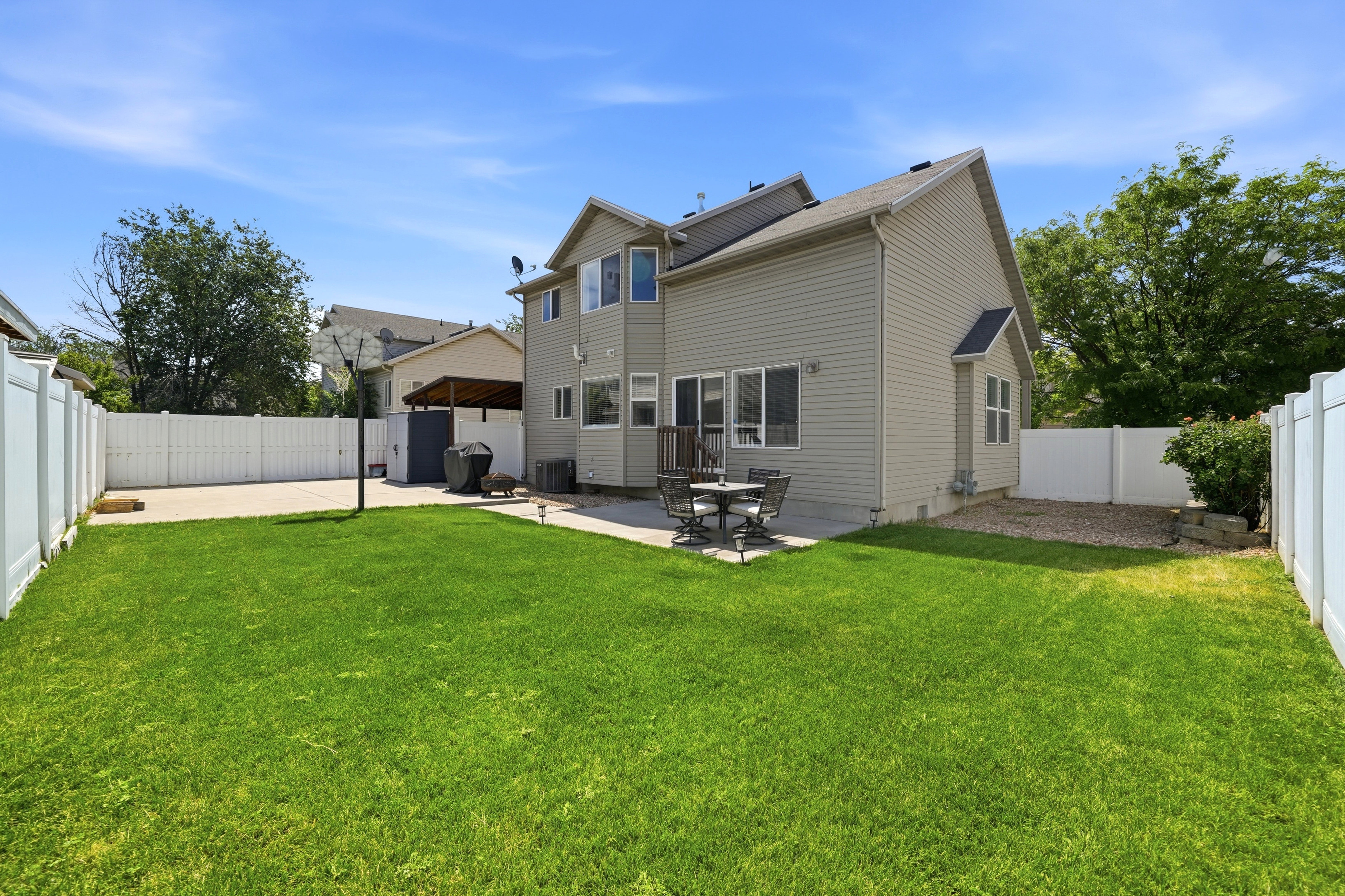 Expansive green lawn with a concrete patio, vinyl fencing, and a gravel bed