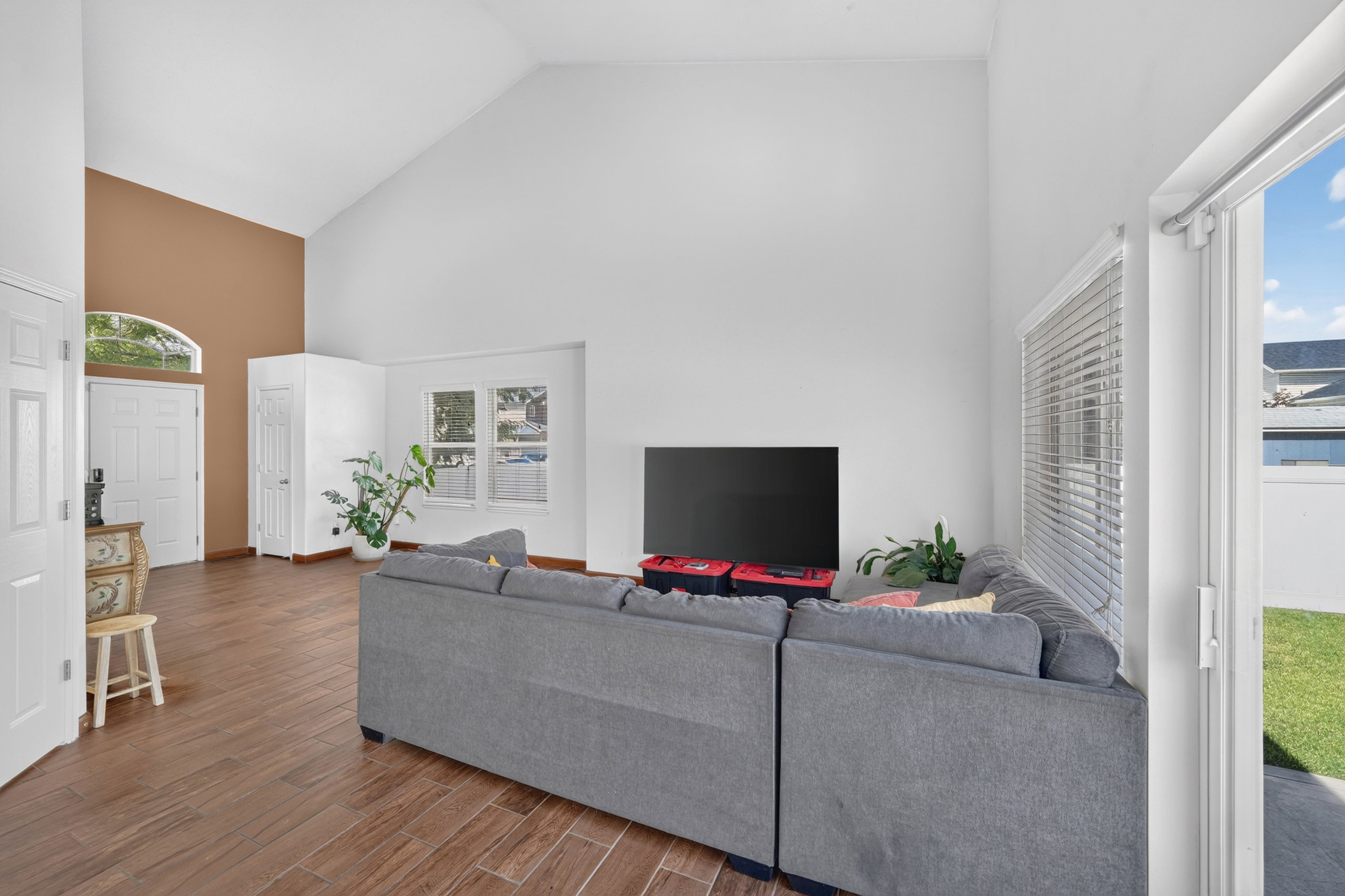 Spacious living area featuring high vaulted ceilings, wood-finish flooring, a sliding glass door providing access to the outdoors, and an arched transom window above the entry door