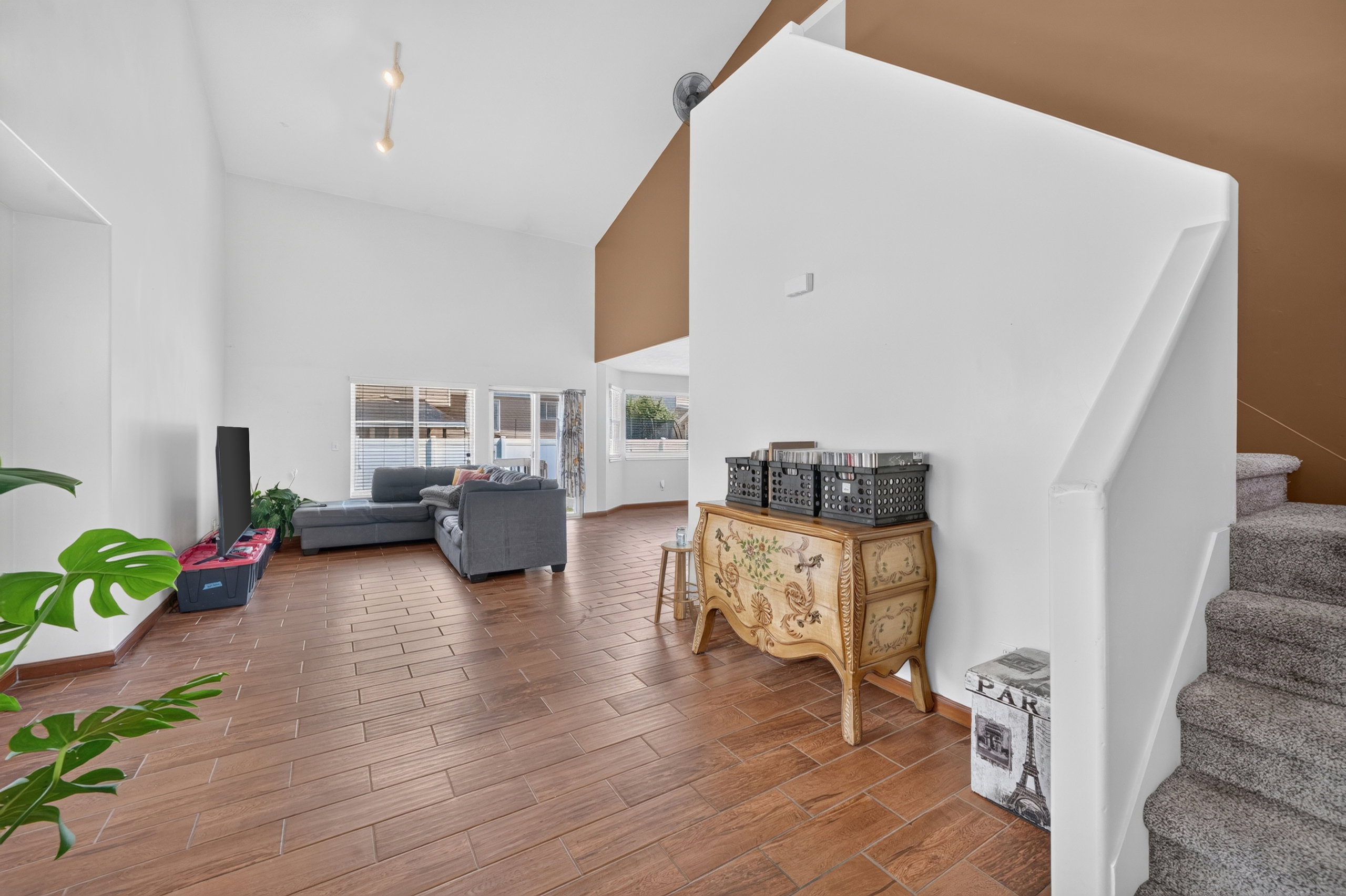 Spacious interior featuring high vaulted ceilings, wood-finish tile flooring, and a broad staircase with carpeted treads