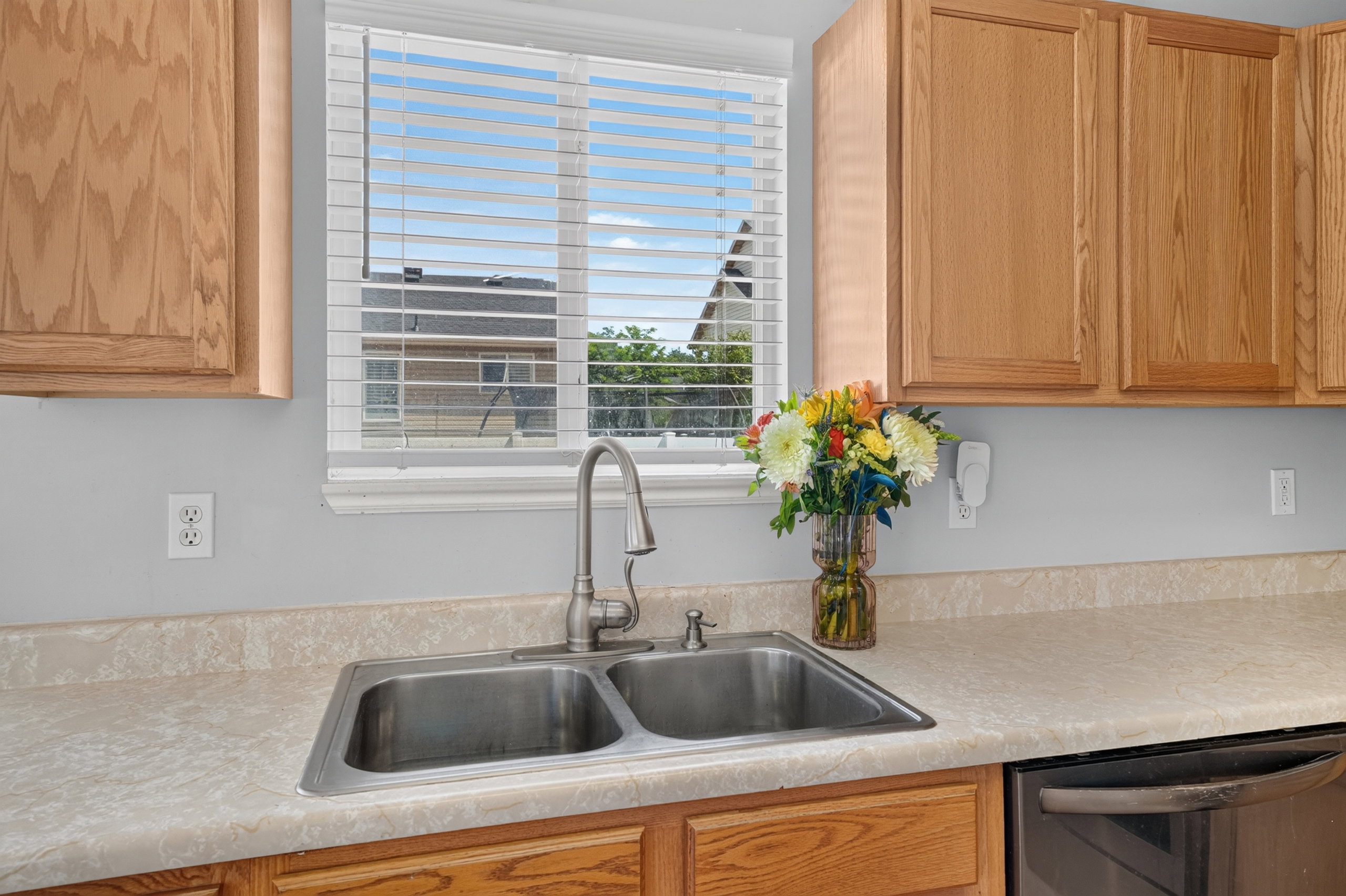 Kitchen sink area featuring a double basin stainless steel sink, brushed nickel faucet, light-toned laminate countertops, and natural wood cabinetry