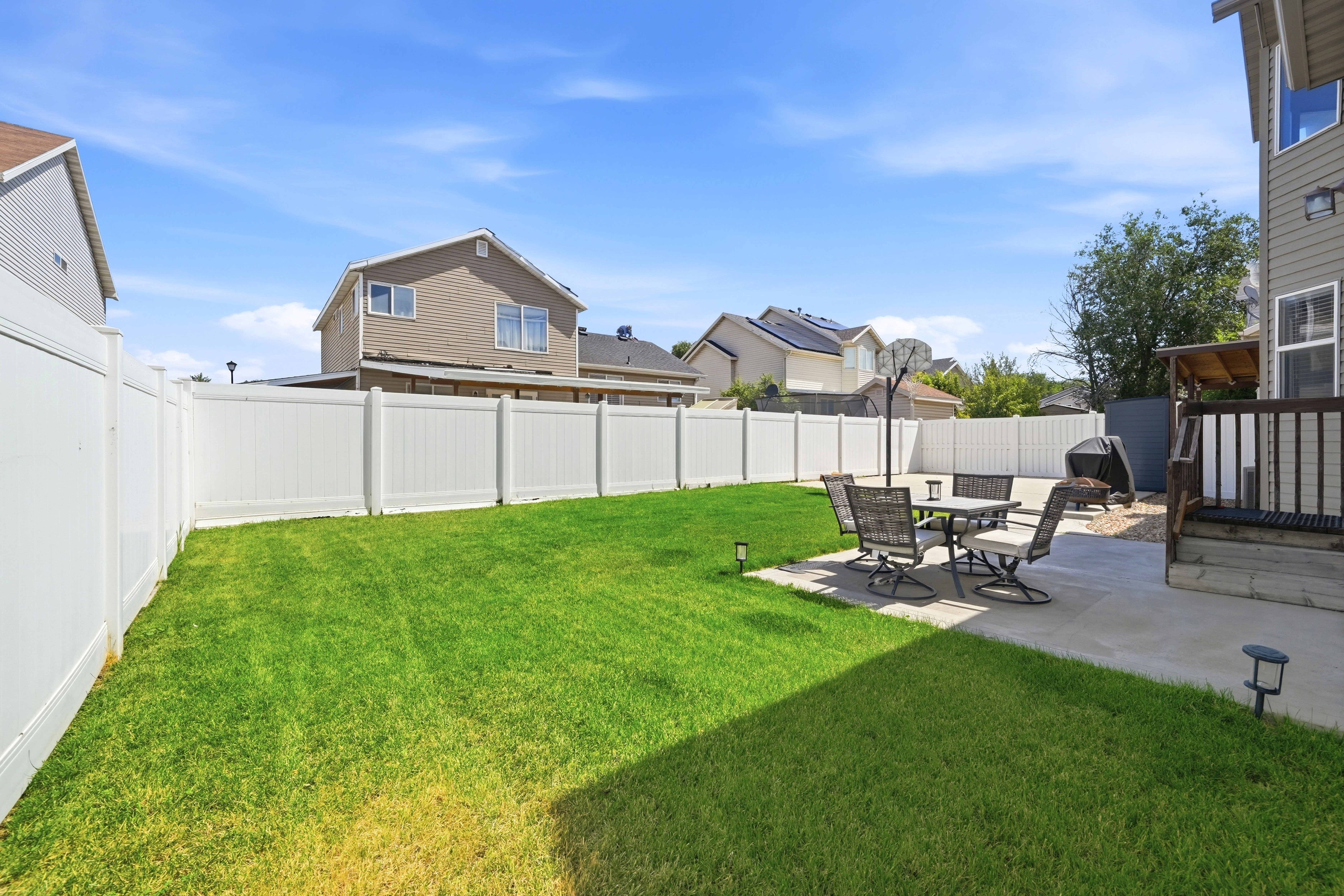 Expansive backyard featuring a green lawn, white vinyl privacy fencing, and a concrete patio