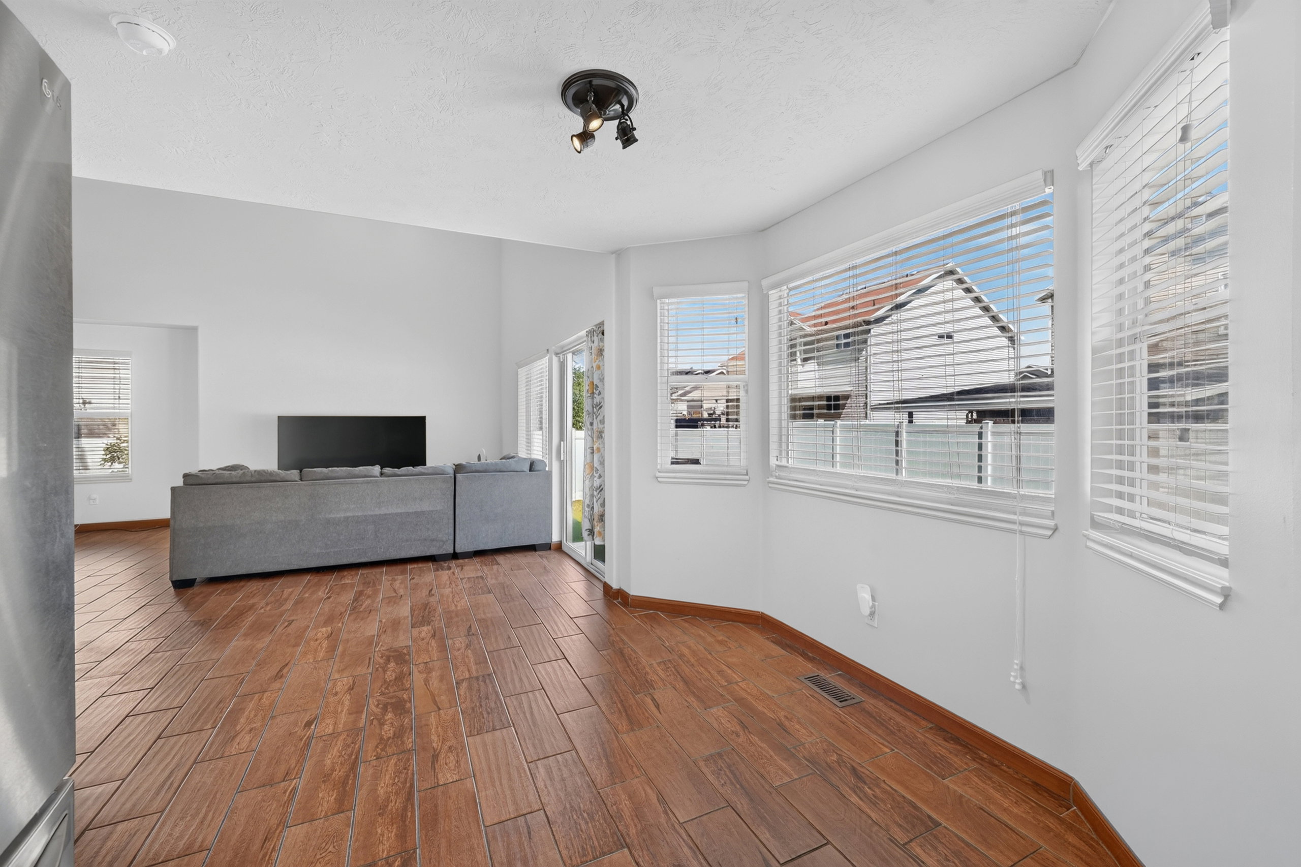 Light-filled living space featuring wood-finish flooring, a contemporary ceiling light fixture, and multiple windows with blinds