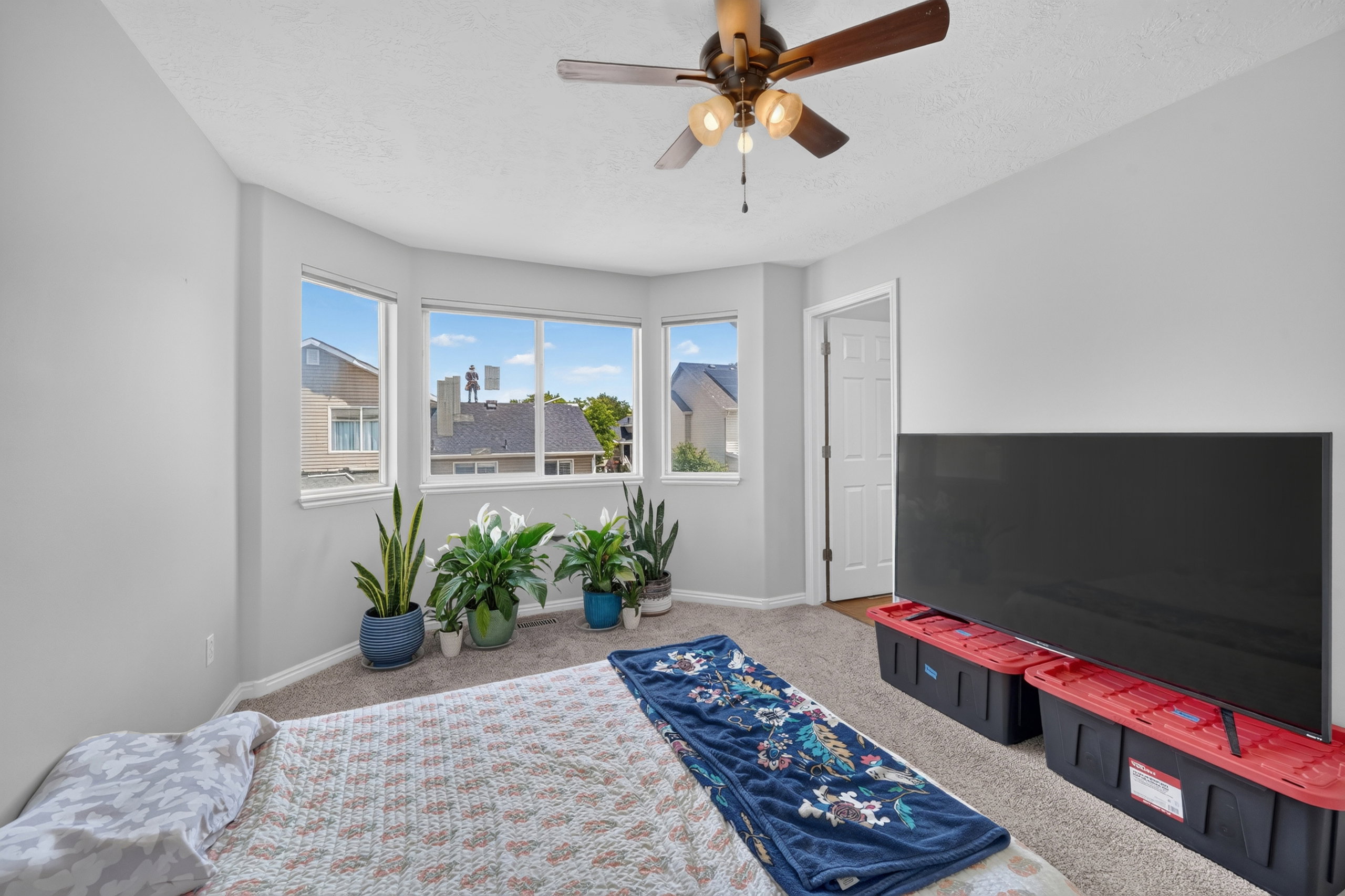 Bay window with multiple panes of glass, a ceiling fan with light fixture, light gray wall paint, and beige carpeting