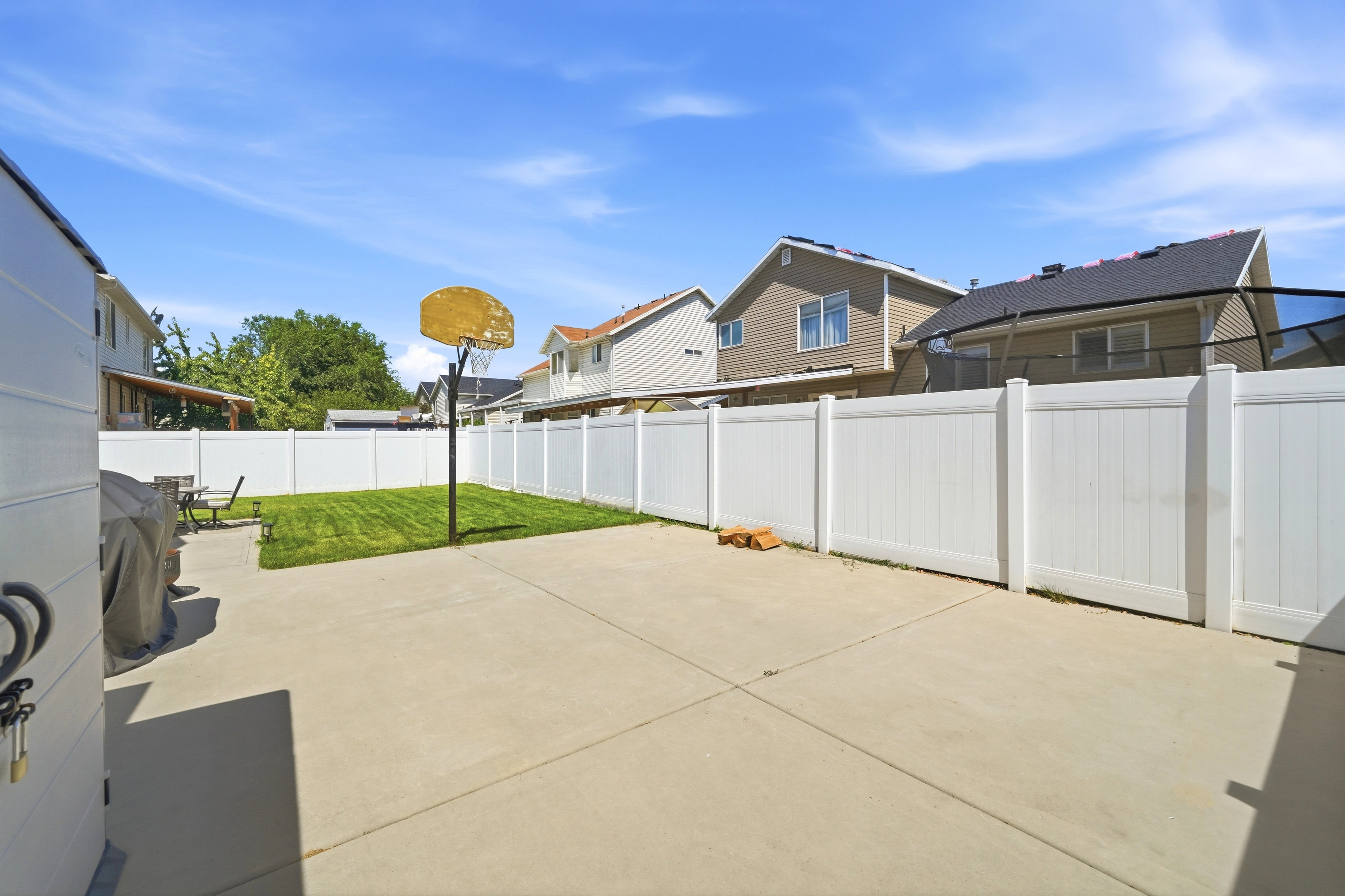 Expansive concrete patio area with a green lawn section and white privacy fencing