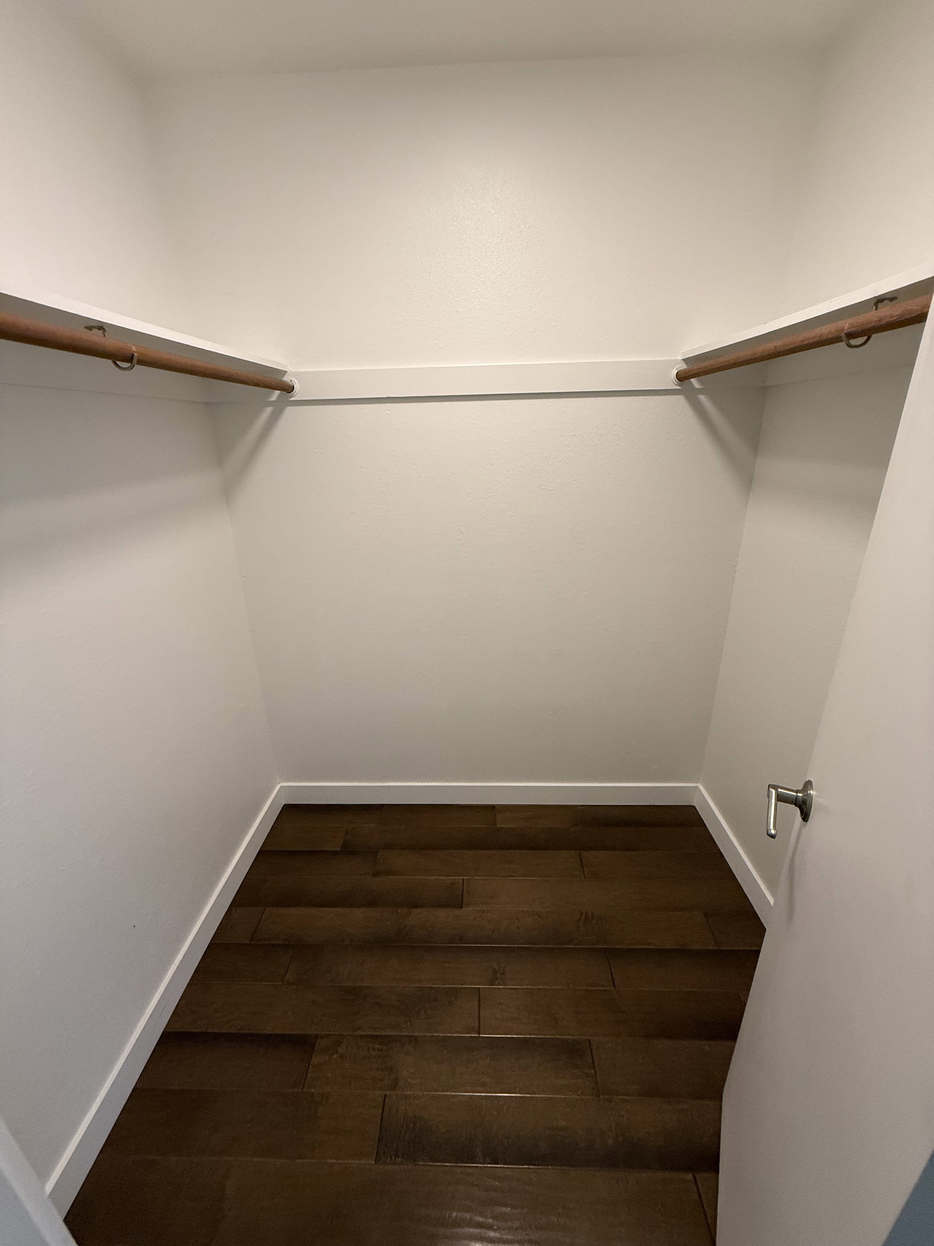 Walk-in closet featuring wood-finish flooring, white baseboards, and two wood-toned hanging rods with white shelving