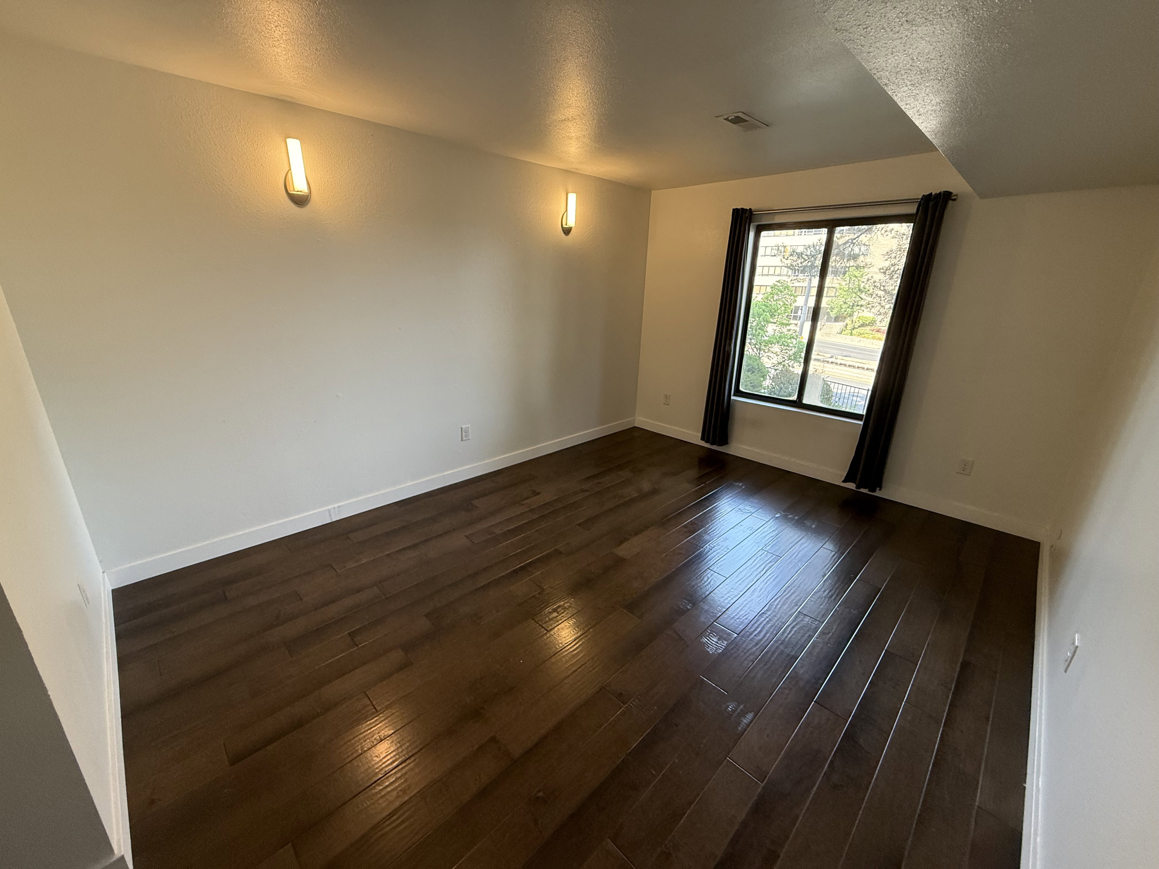 Room featuring dark wood-finish flooring, white walls, and a window with dark curtains