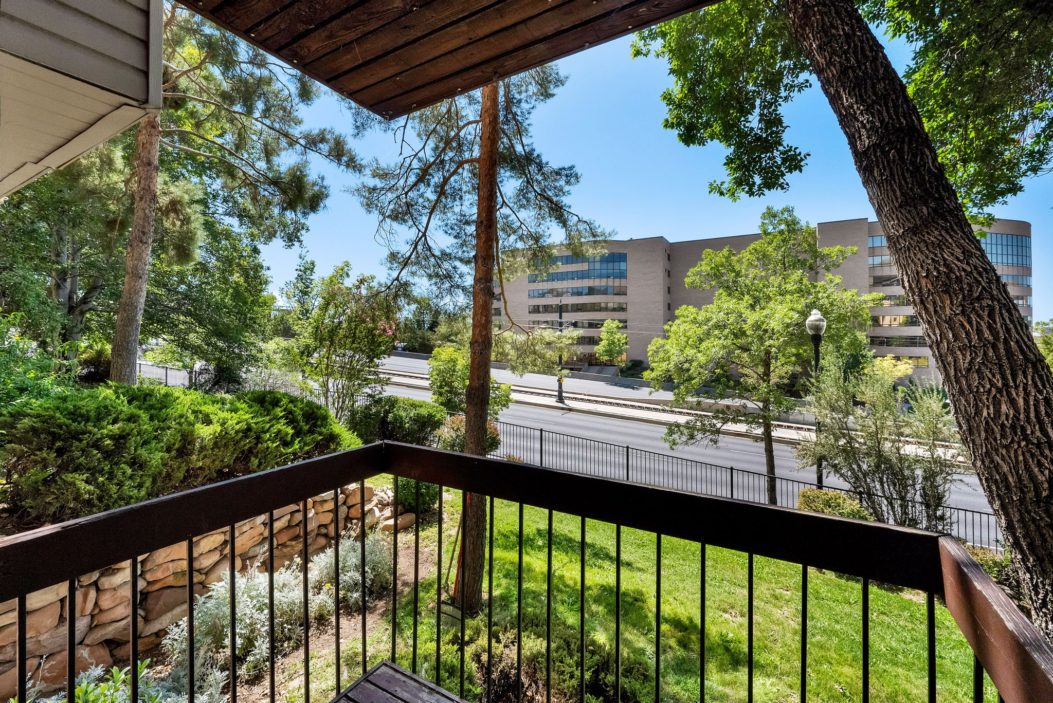 Balcony with dark-finish railing and wood-finish ceiling, overlooking a landscaped area with mature trees and shrubs