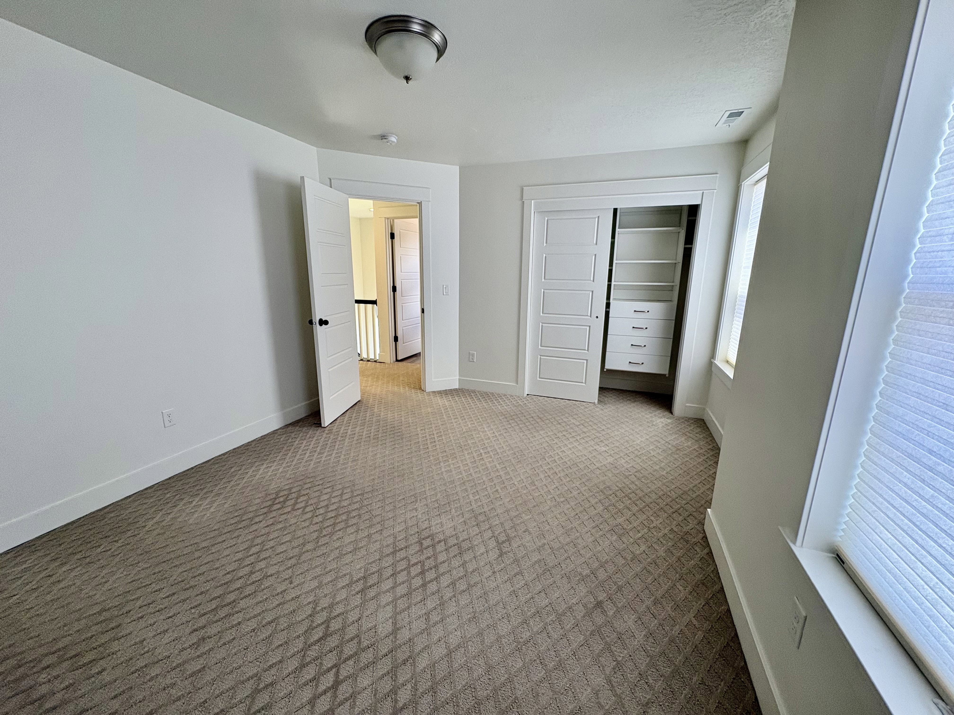 Bright room featuring patterned carpet flooring, white walls, and a window with blinds