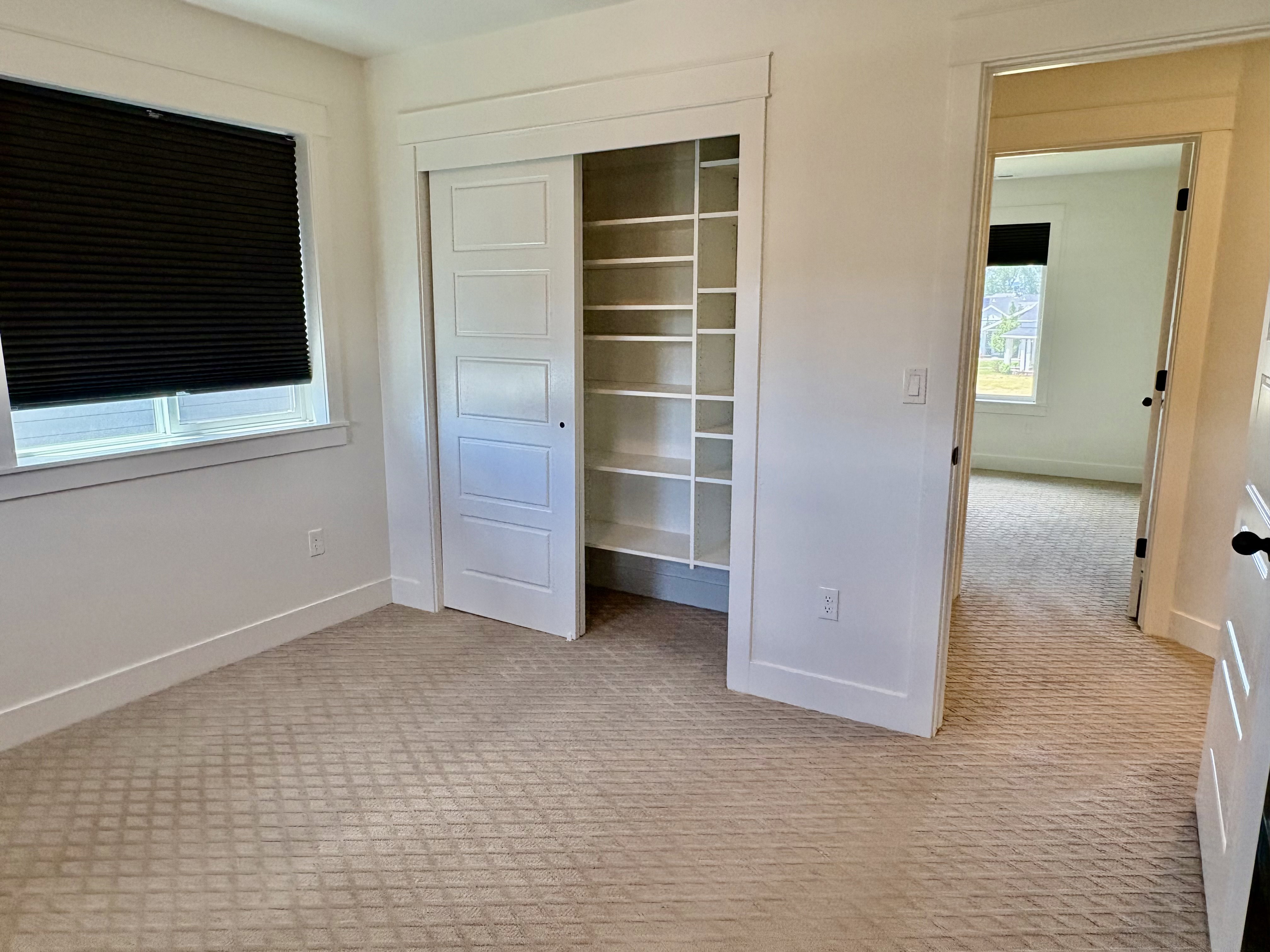 Room featuring patterned carpeting, white walls, and a window with a black cellular shade