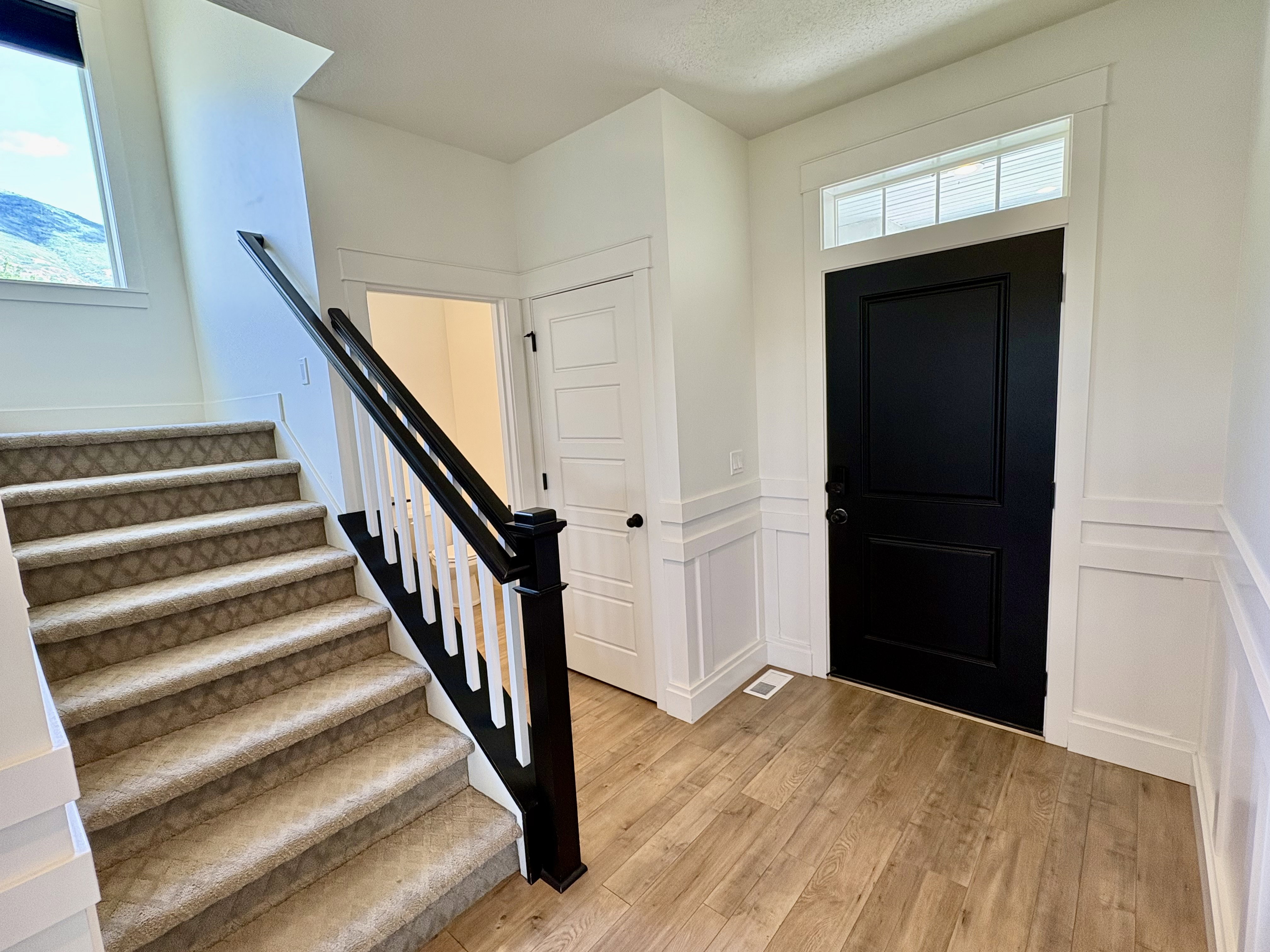 Entryway featuring wood-finish flooring, white wainscoting, and a dark paneled door with a transom window