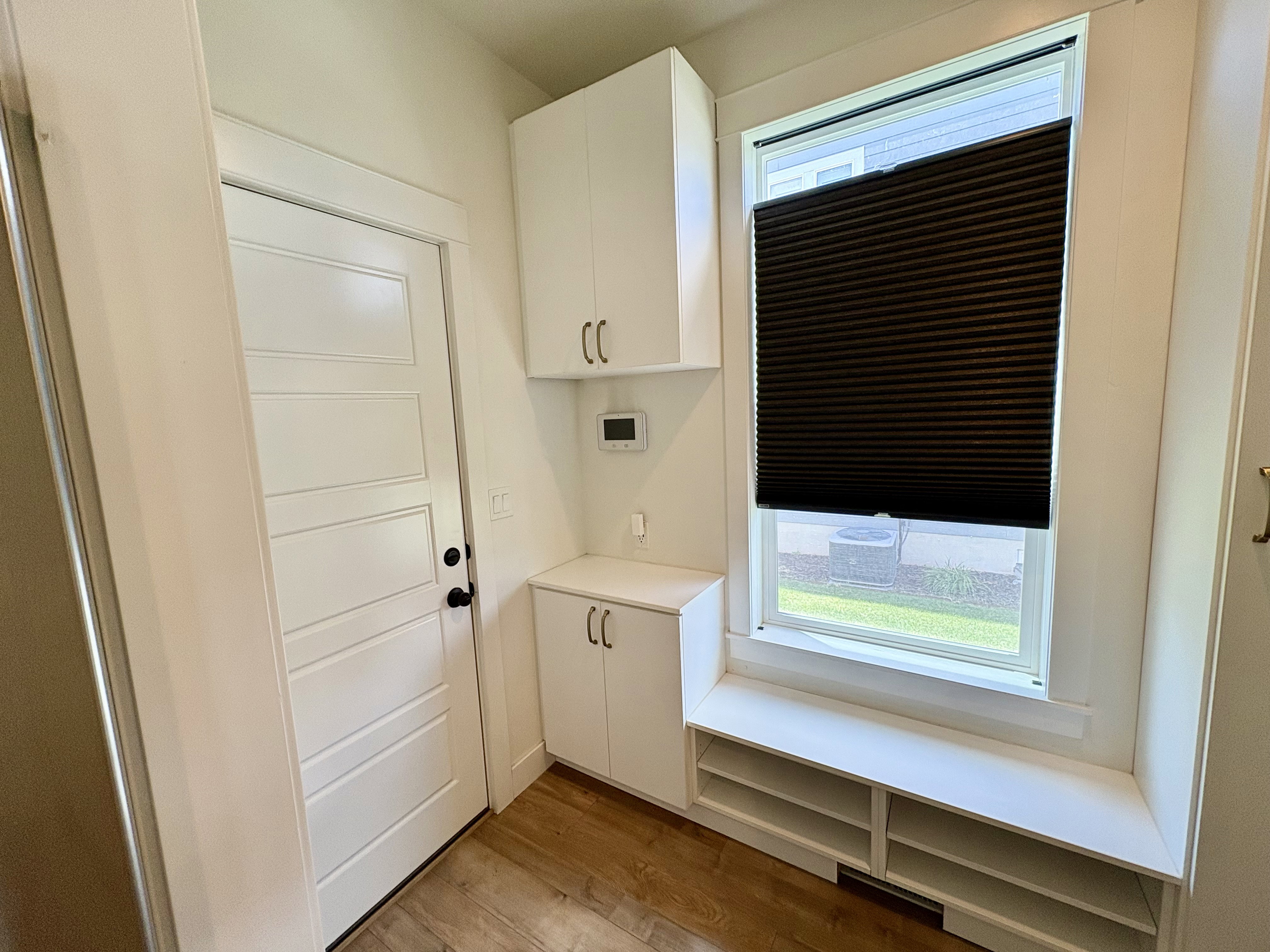 Entry area featuring wood-finish flooring, white paneled door, built-in white cabinetry, window with privacy blind, and a built-in bench with integrated shelving