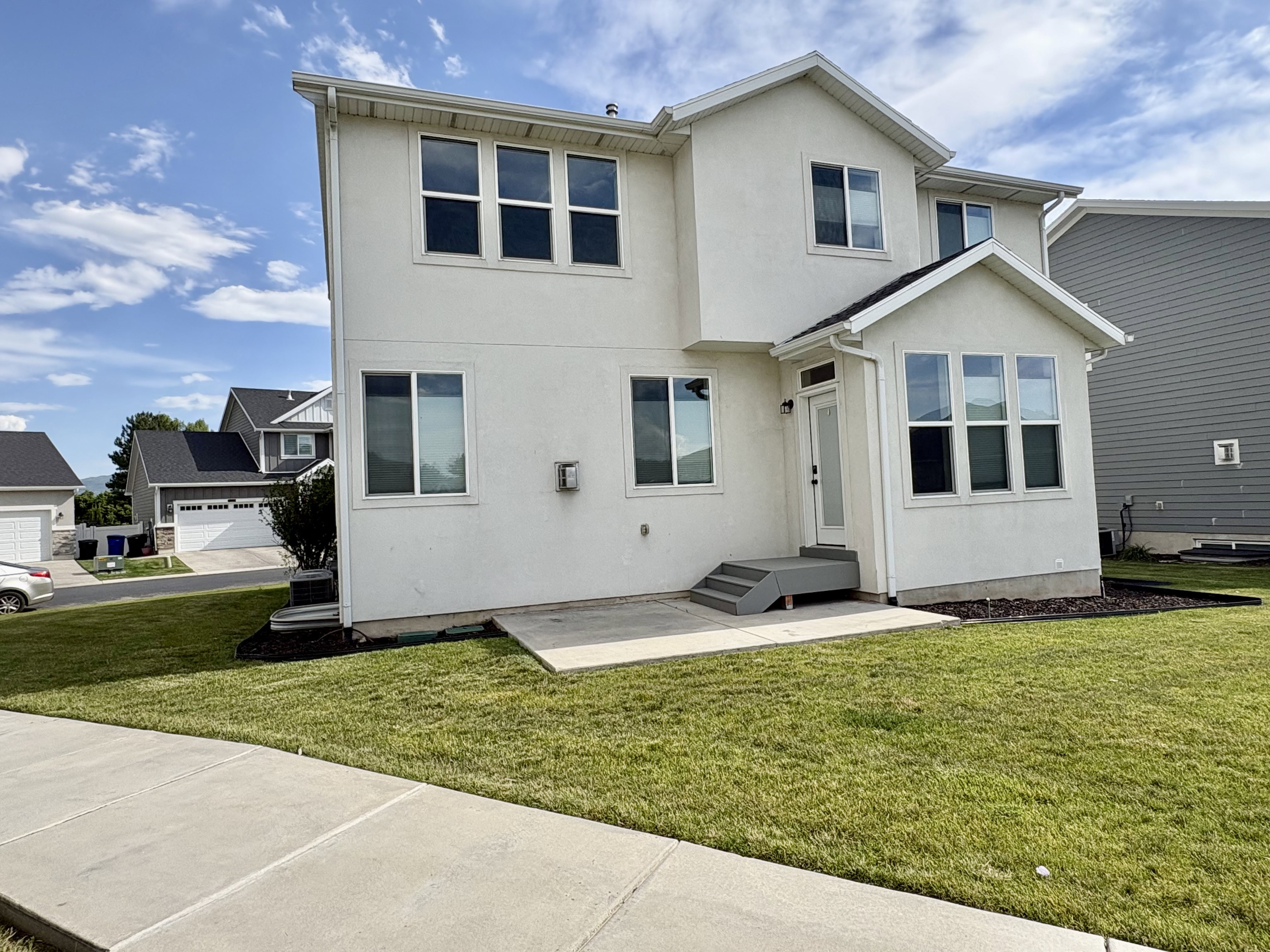 Rear exterior featuring a sunroom addition with multiple windows, stucco siding, a ground-level patio, and a tiered deck with steps