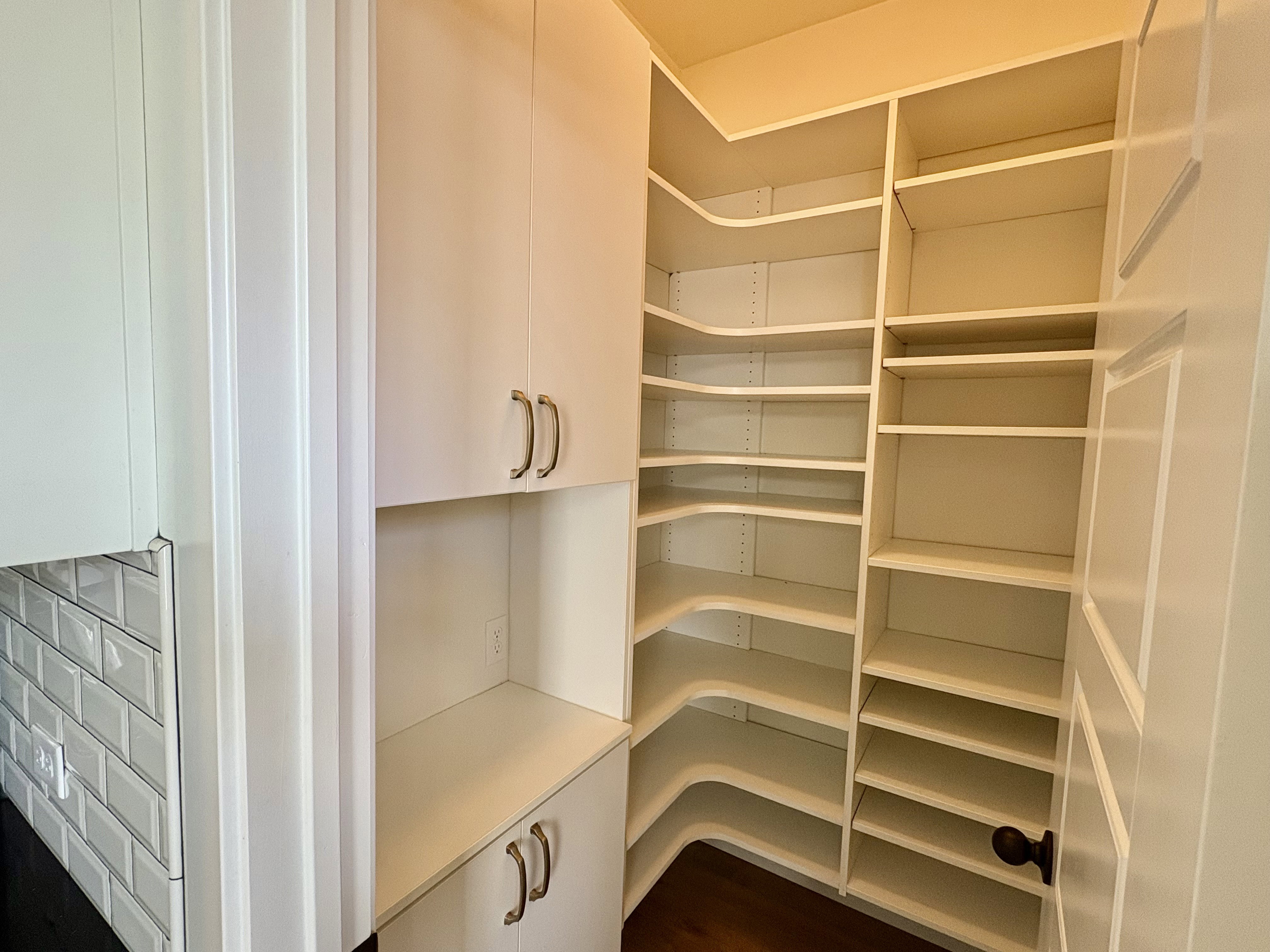 Walk-in pantry featuring expansive shelving, built-in cabinetry with silver-tone hardware, and a dark wood-finish floor