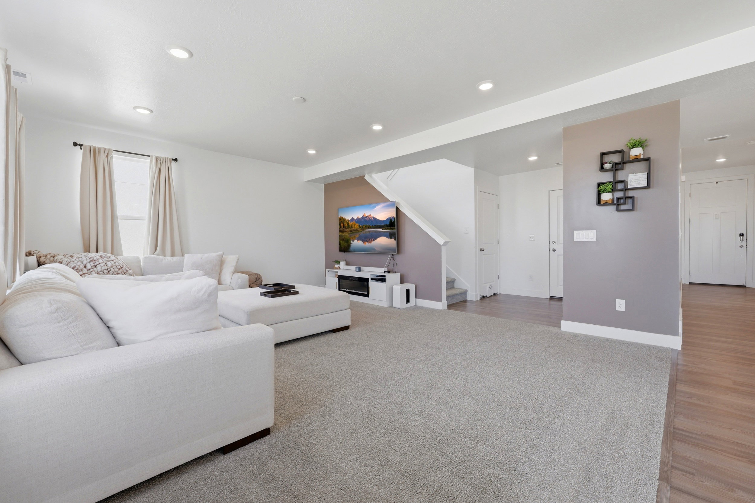 Open-concept living area featuring light-colored carpeting, recessed lighting, a neutral wall color, a window with natural light, and wood-finish flooring extending into the entryway